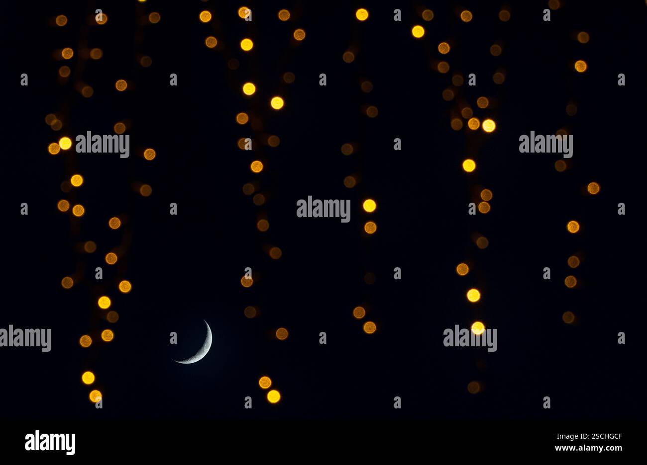 Una tranquilla luna crescente brilla sotto un baldacchino di luci scintillanti dorate nel cielo notturno, creando un'atmosfera da sogno e serena. Foto Stock