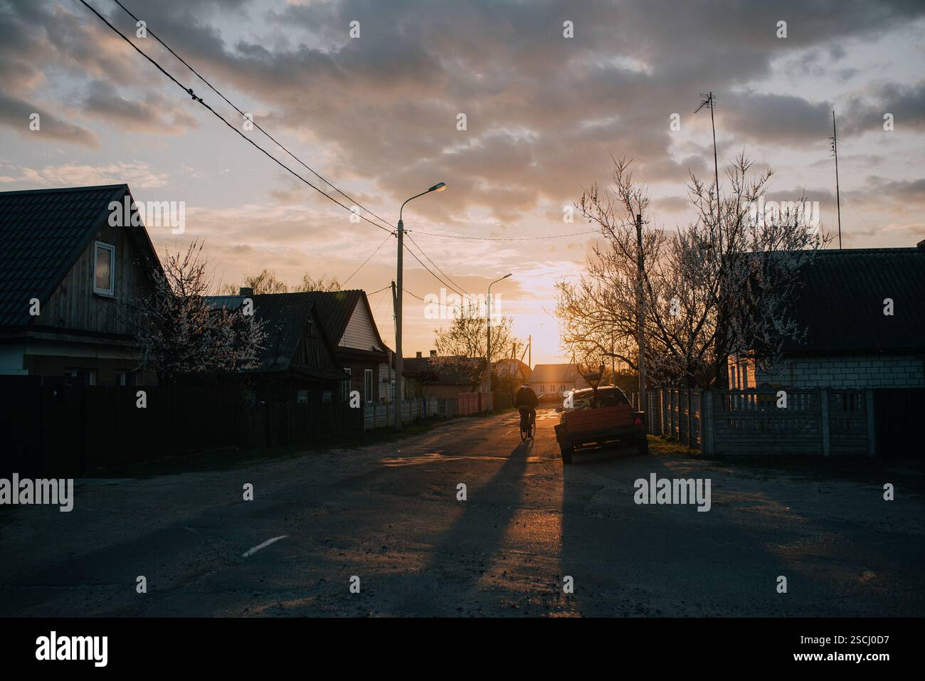 La sagoma di un uomo in bicicletta attraverso un villaggio rurale dell'Europa orientale al tramonto Foto Stock