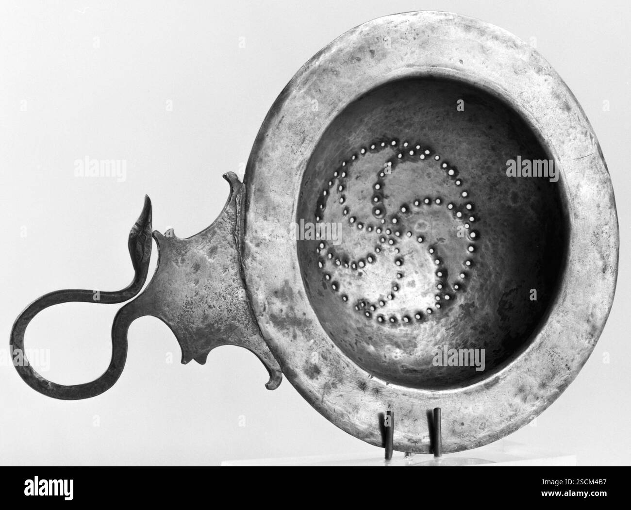 Sainer, IV secolo a.C. Ulteriori informazioni: Un filtro a forma di ciotola con labbro largo e piatto e manico a forma di collo e testa di cigno. Il recipiente e l'impugnatura sono composti da due pezzi di metallo separati. Le perforazioni sul fondo della ciotola sono disposte secondo un modello circoscritto di stelle marine vorticose. L'incisione viene utilizzata per gli occhi del cigno. Foto Stock