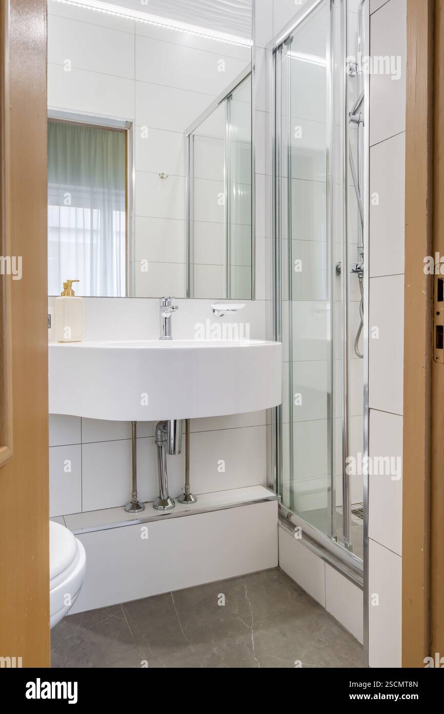 Bagno luminoso ed elegante con box doccia in vetro, WC a parete e piastrelle effetto marmo per un aspetto elegante e lussuoso. Foto Stock