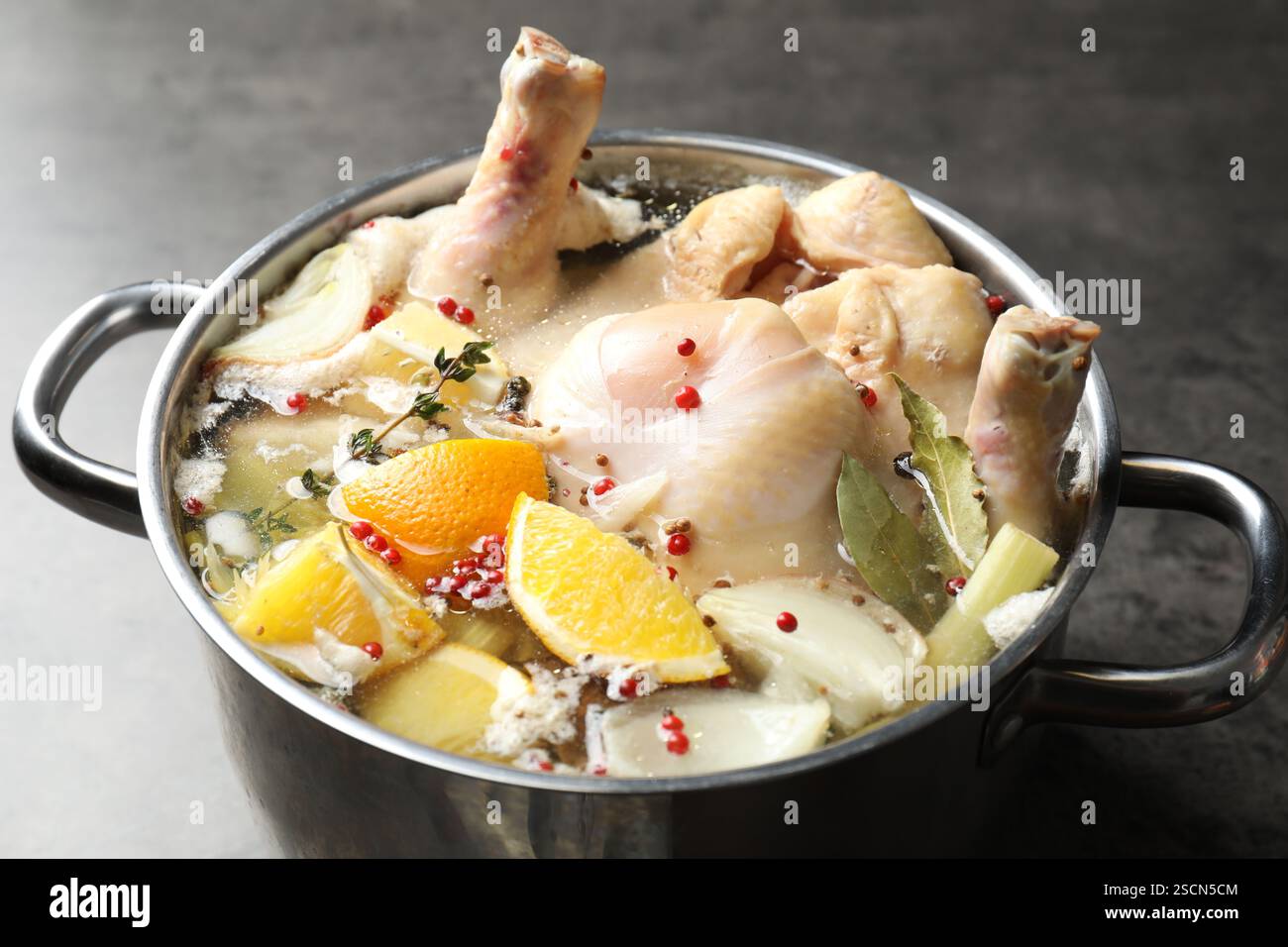 tacchino intero, agrumi tagliati e spezie in pentola su tavola grigia, primo piano Foto Stock