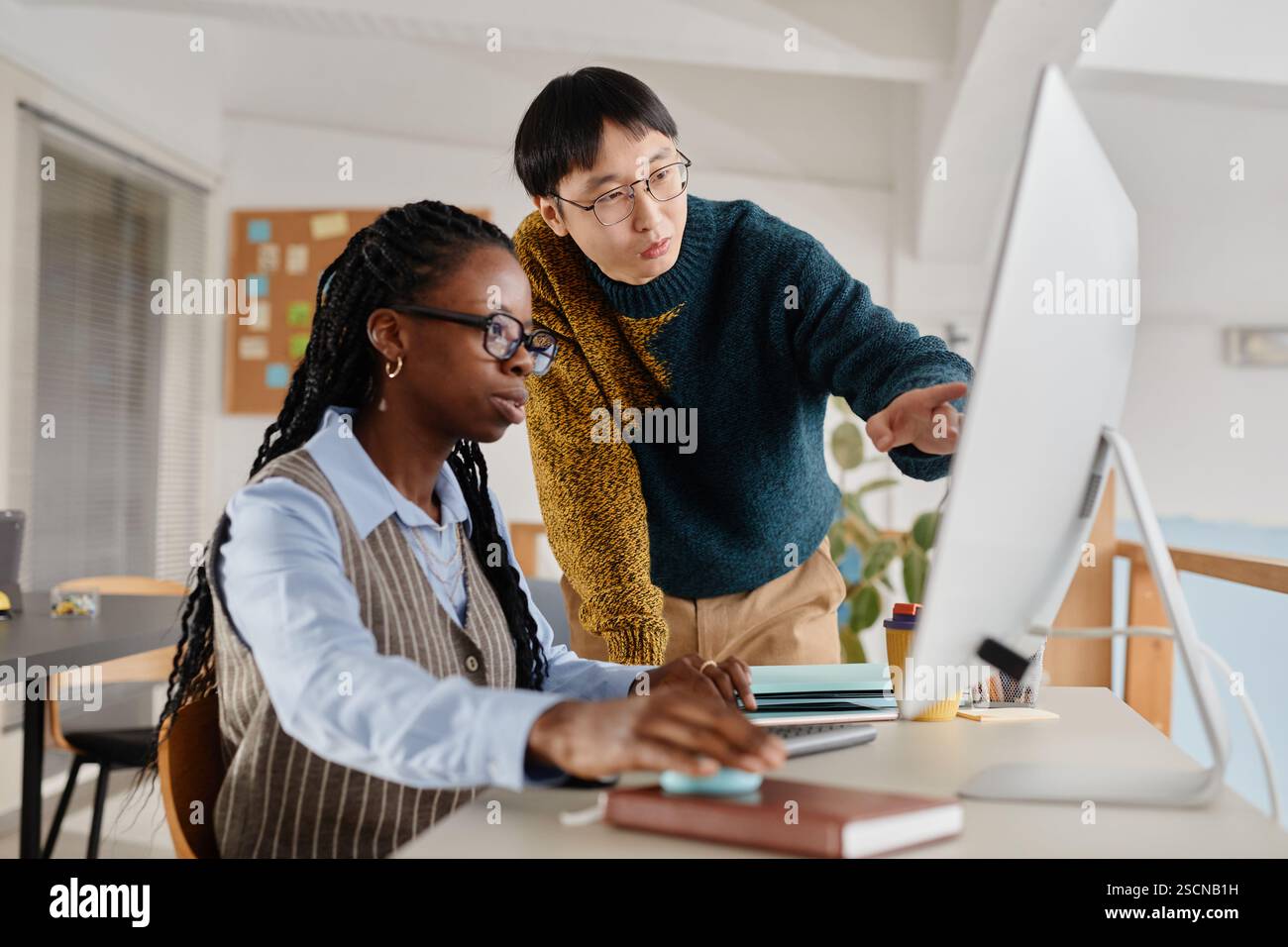 Due colleghi che analizzano i dati su uno schermo di un computer in un ufficio, impegnati in un lavoro collaborativo. Uno indossa gli occhiali osservando attentamente mentre spiega i dettagli Foto Stock