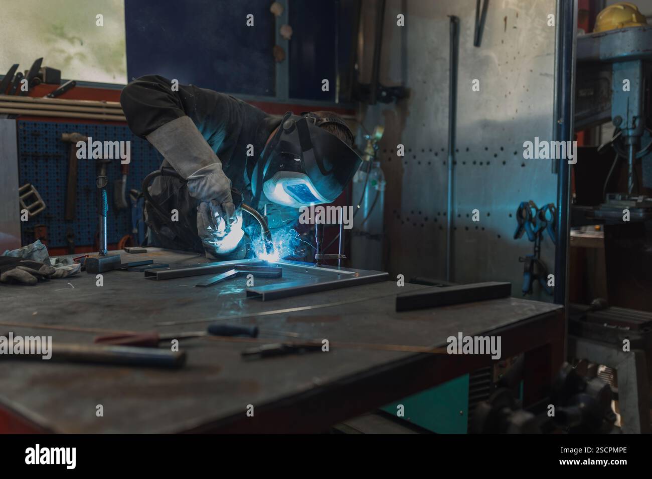 Saldatrice MIG indossando indumenti e dispositivi di protezione individuale per la saldatura e lavorando in un'officina. Concetti di assistenza, industria e fabbricazione Foto Stock