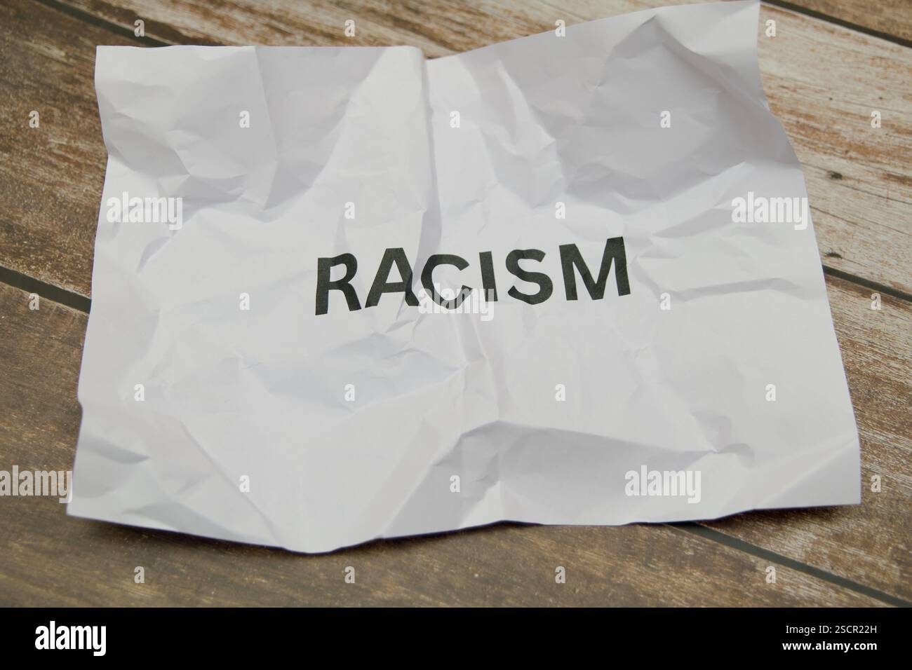 Un foglio di carta sgualcito mostra la parola razzismo in grassetto su uno sfondo di legno testurizzato. Foto Stock