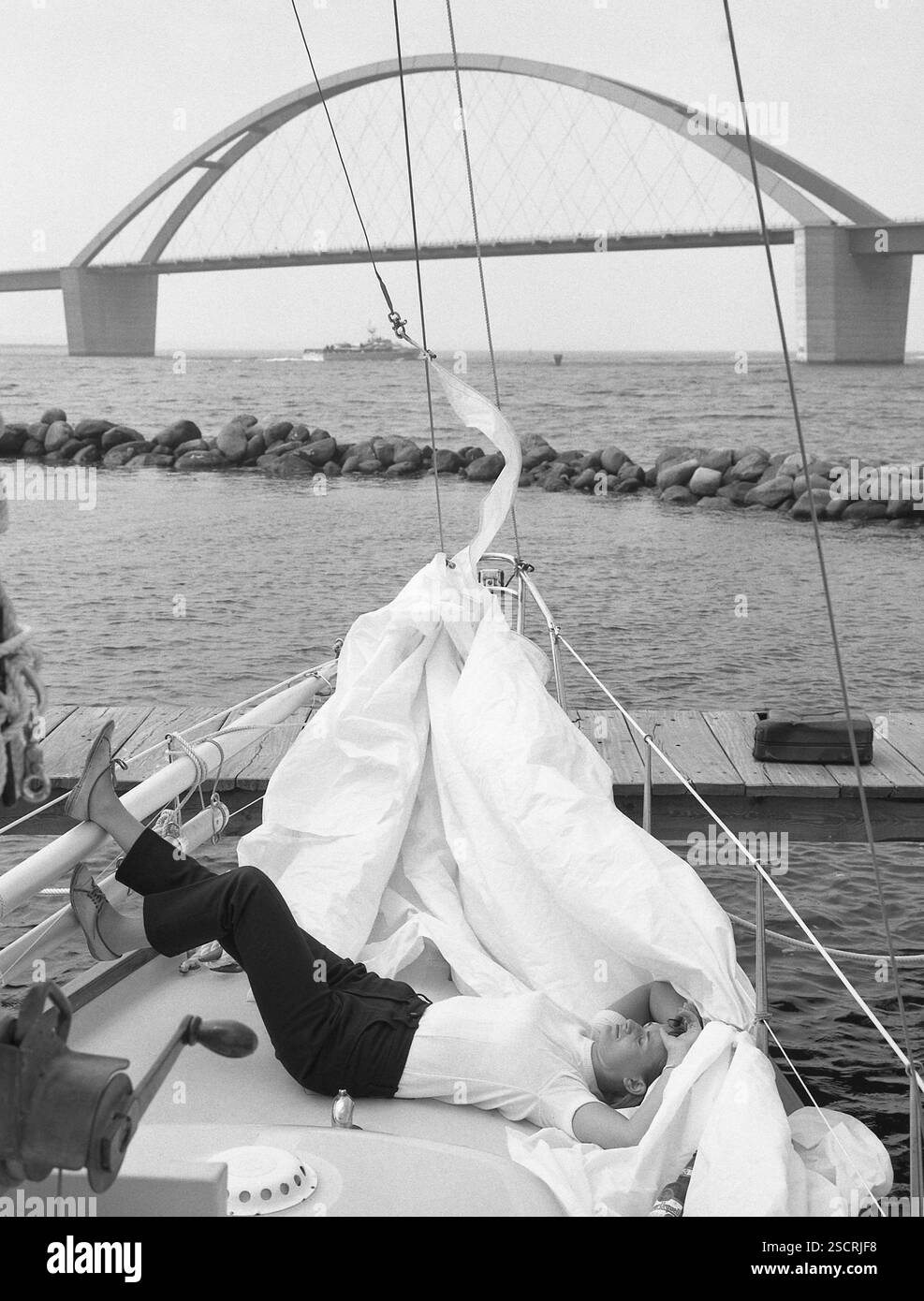 Una donna giace su una nave a vela. La tela accanto a lei e il Ponte Fehmarnsund sullo sfondo. [traduzione automatizzata] Foto Stock