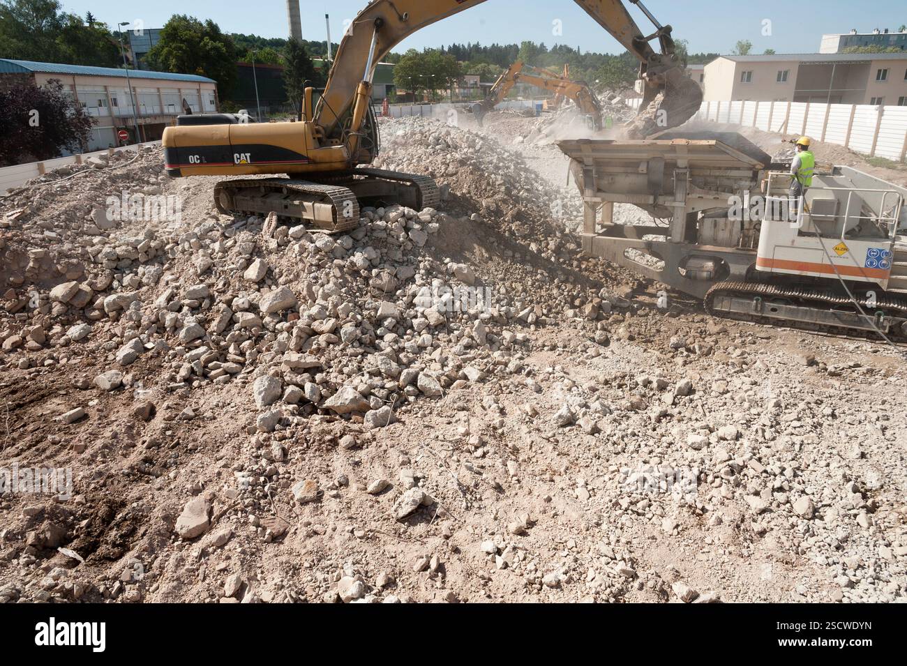 In un cantiere di decostruzione, una pala meccanica fornisce un frantumatore mobile. Foto Stock