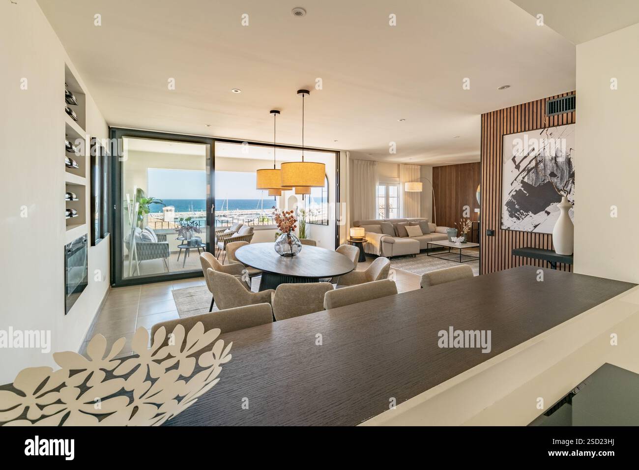 Un'immagine di un soggiorno aperto e di una sala da pranzo con balcone aperto che si affaccia sulla città portuale di Puerto Banus Foto Stock