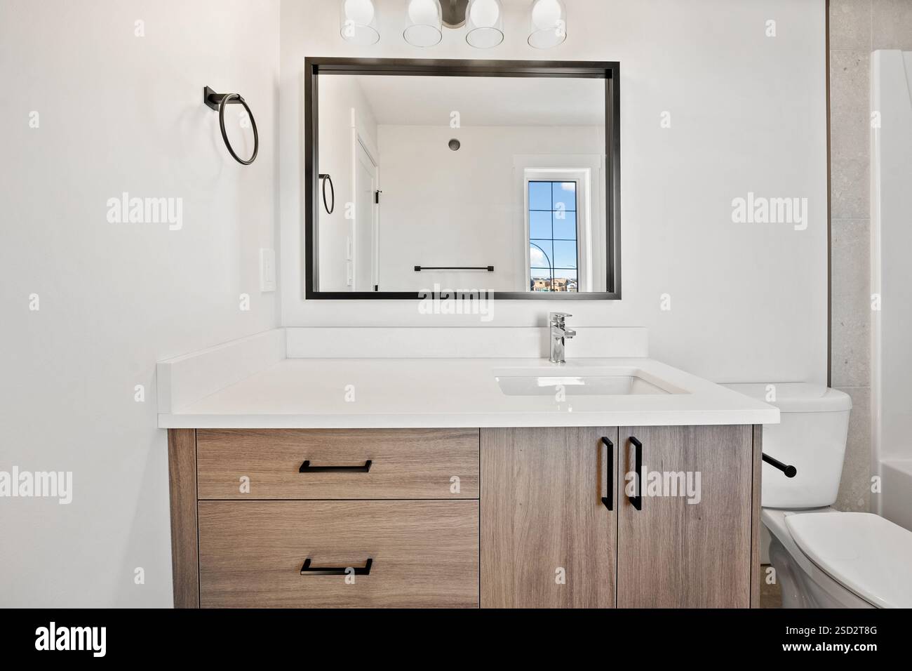 Bagno con lavandino bianco, WC e specchio sopra il lavandino. Lo specchio è incorniciato in nero e ha un rubinetto d'argento. Il bagno era pulito e pulito Foto Stock