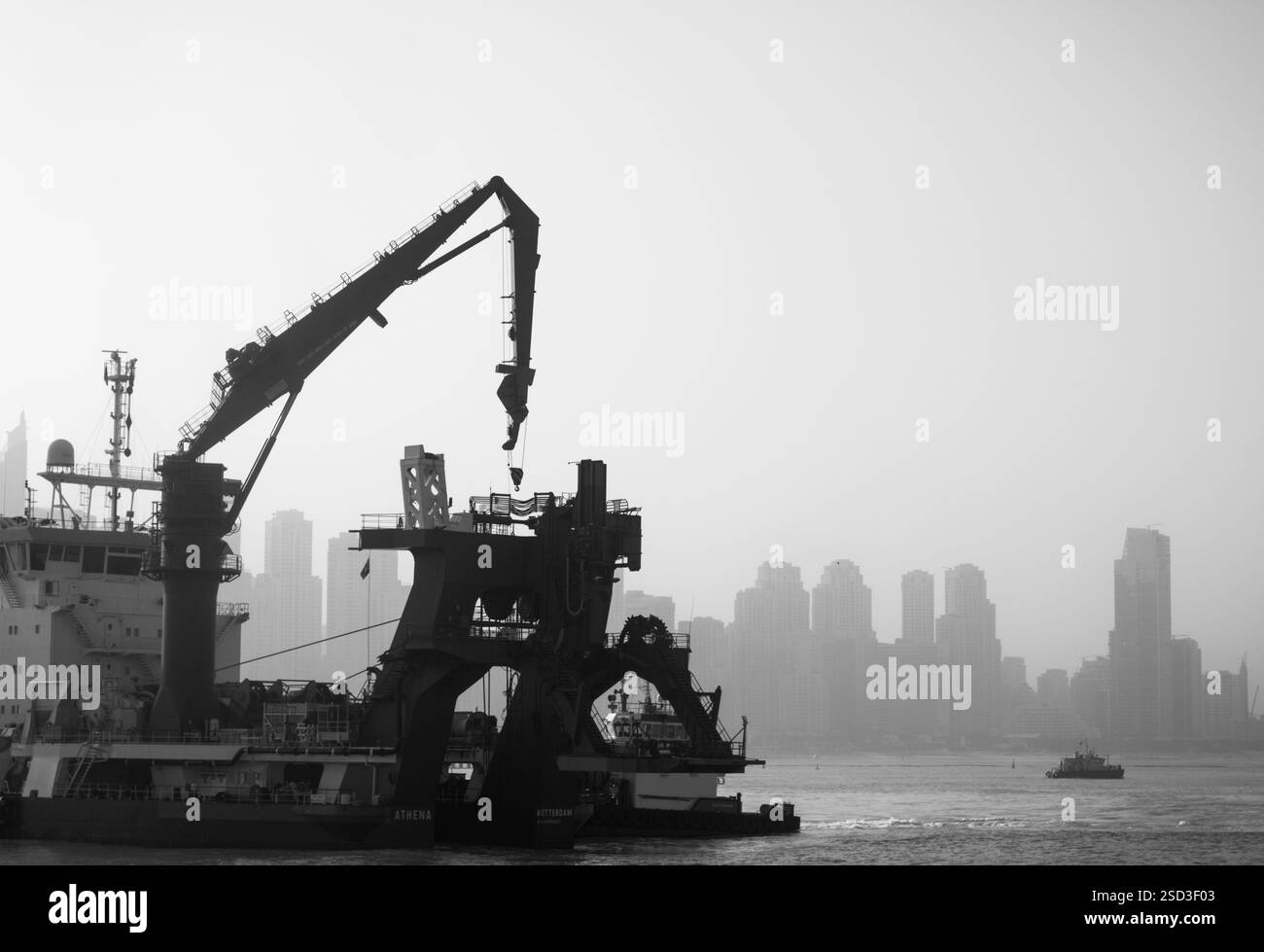 Nave industriale sagomata con gru contro lo skyline nebuloso della città in bianco e nero Foto Stock