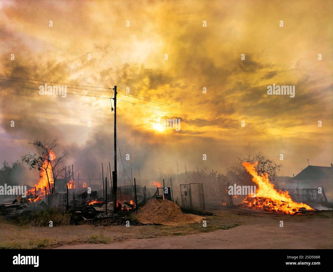 Fuoco e casa bruciata in un villaggio al tramonto Foto Stock
