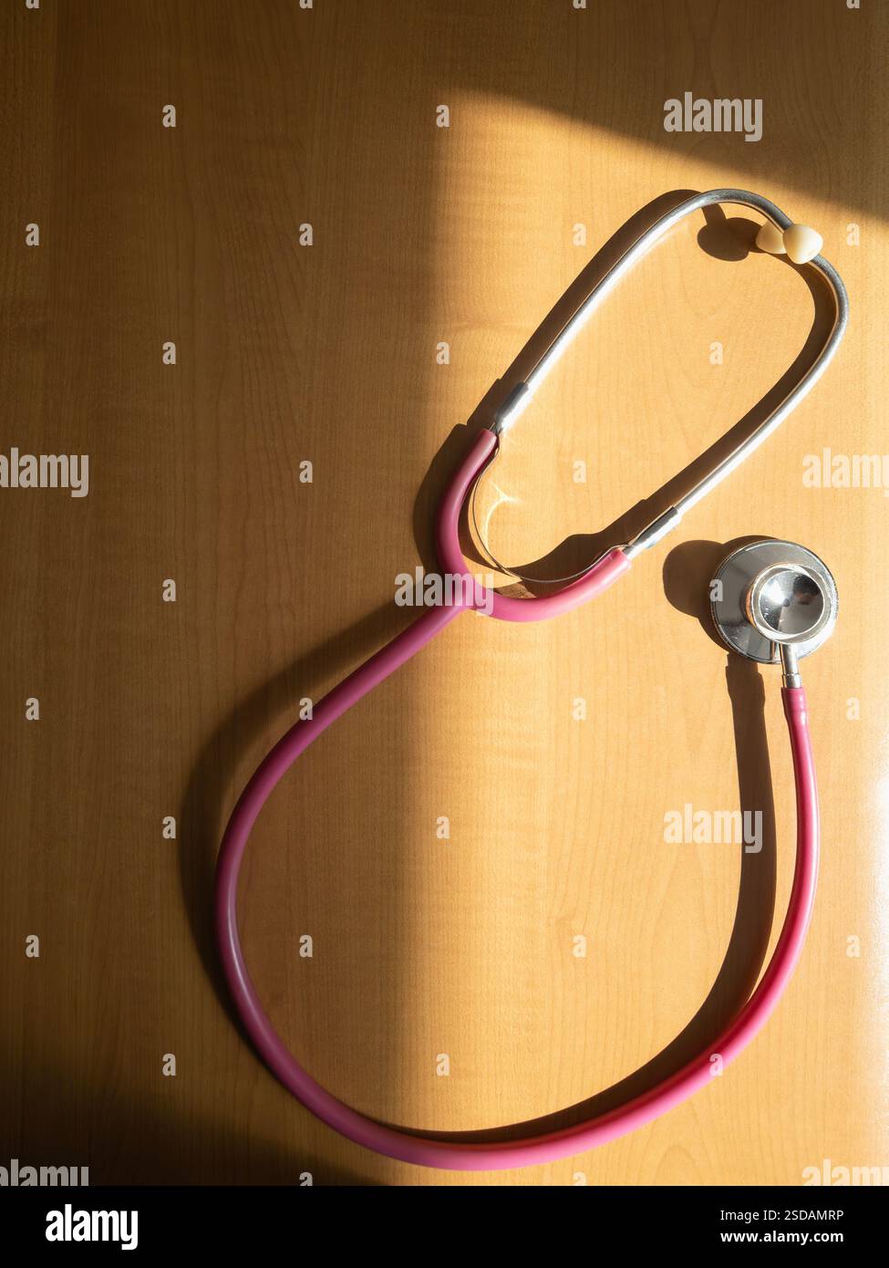 Stetoscopio rosa su un tavolo di legno alla luce del sole - Immagine stock catturata con smartphone