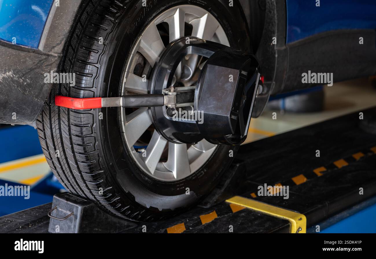 L'attrezzatura di allineamento delle ruote afferra lo pneumatico della ruota di un'officina di riparazione. Allineamento automatico delle ruote in officina nella stazione di servizio. Equilibratura ruote auto. Foto Stock