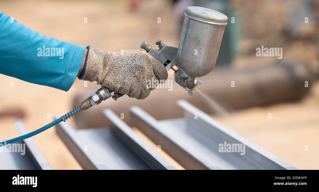 Il lavoratore edile dipinge il rivestimento superficiale della struttura metallica con una pistola a spruzzo in cantiere. Protezione contro la corrosione e la ruggine dei metalli. Industriale Foto Stock
