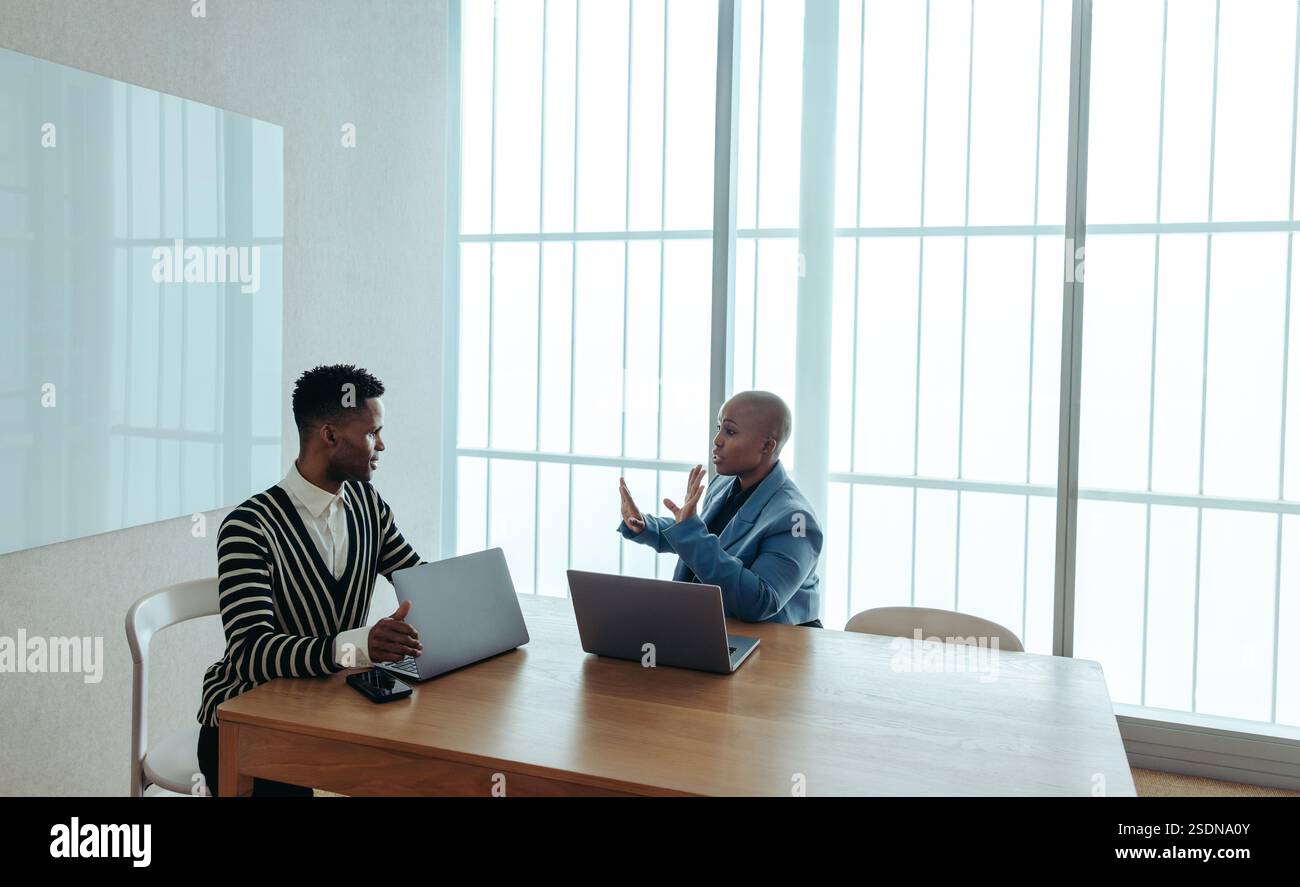 Due professionisti aziendali partecipano attivamente a una sessione di strategia, discutendo importanti argomenti di gestione con i notebook aperti, suggerendo coll Foto Stock