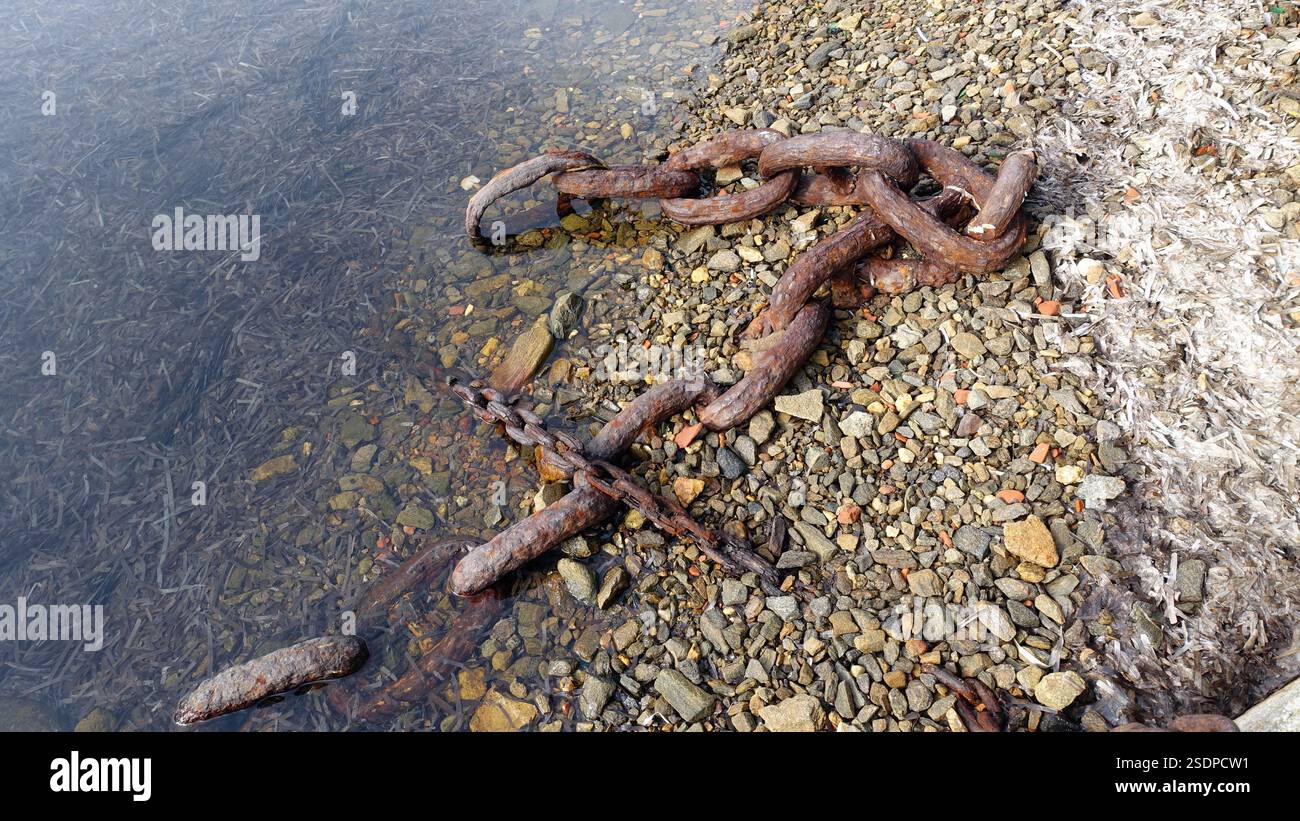 Catene arrugginite abbandonate su una spiaggia rocciosa. Foto Stock