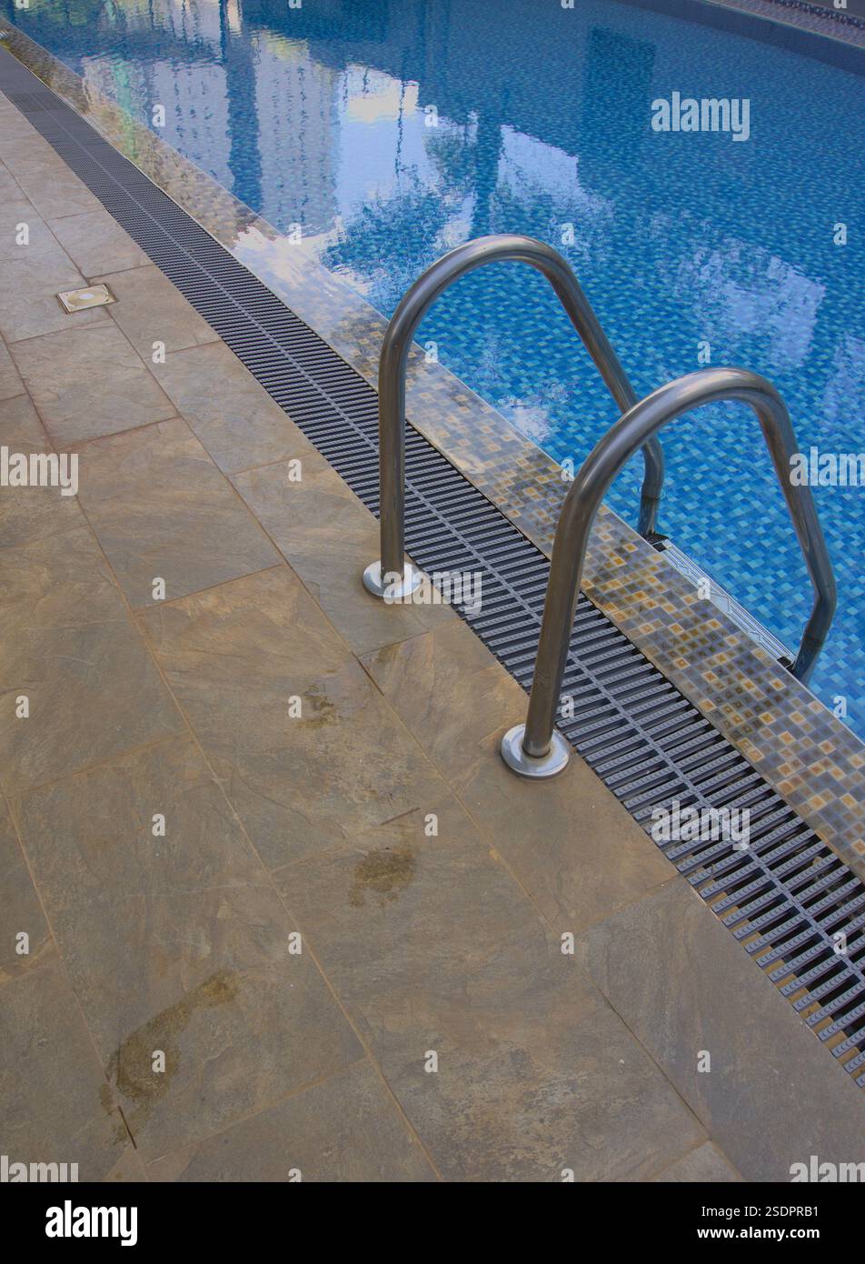 impronte bagnate accanto alla scala accanto alla piscina con acqua limpida Foto Stock