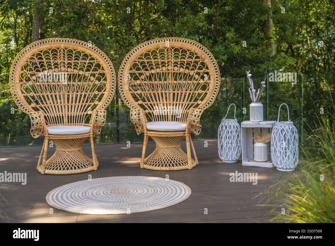 Due sedie di pavone in vimini e decorazioni bianche si stagliano su un ponte di legno, creando un'atmosfera bohémien per una cerimonia di nozze Foto Stock