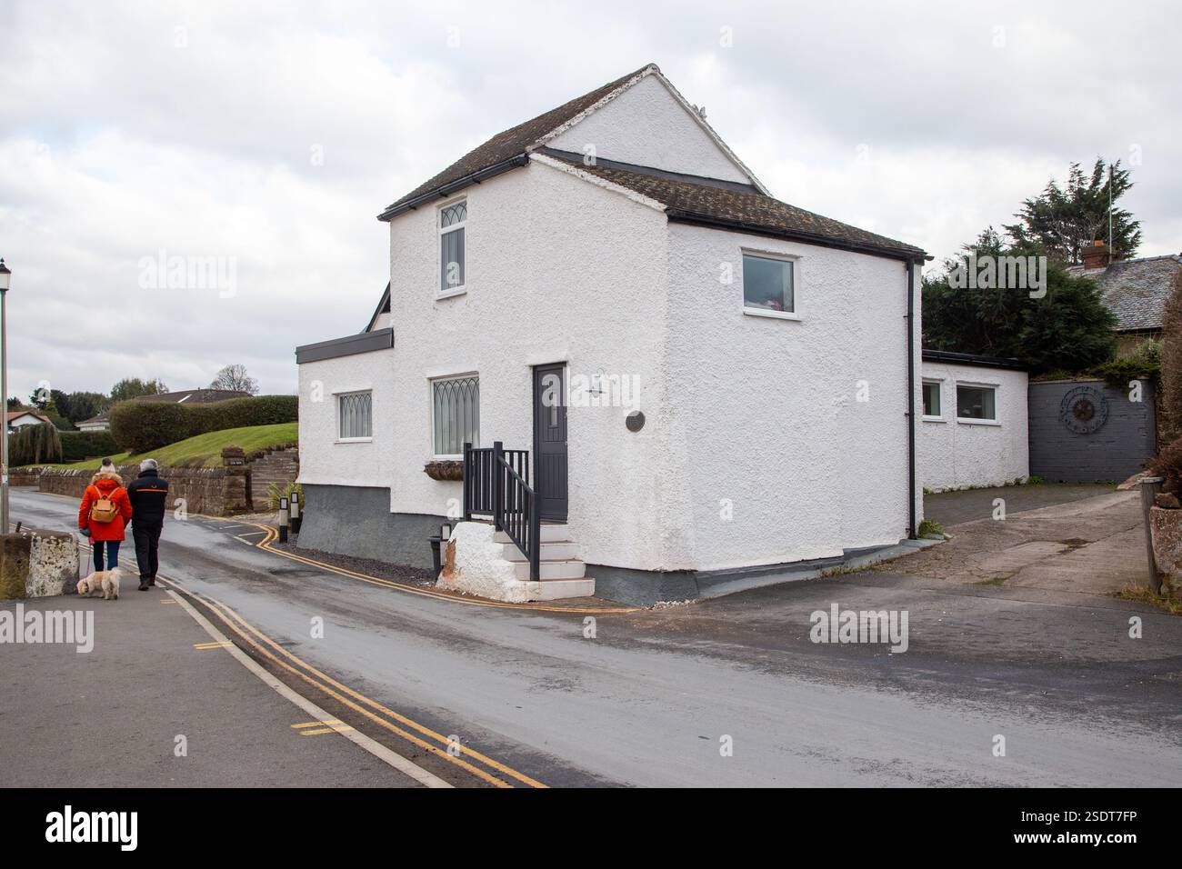 Una coppia passeggia davanti alla vecchia casa di orologi risalente al 1720, ex casa doganale nel villaggio wirral di Parkgate Foto Stock