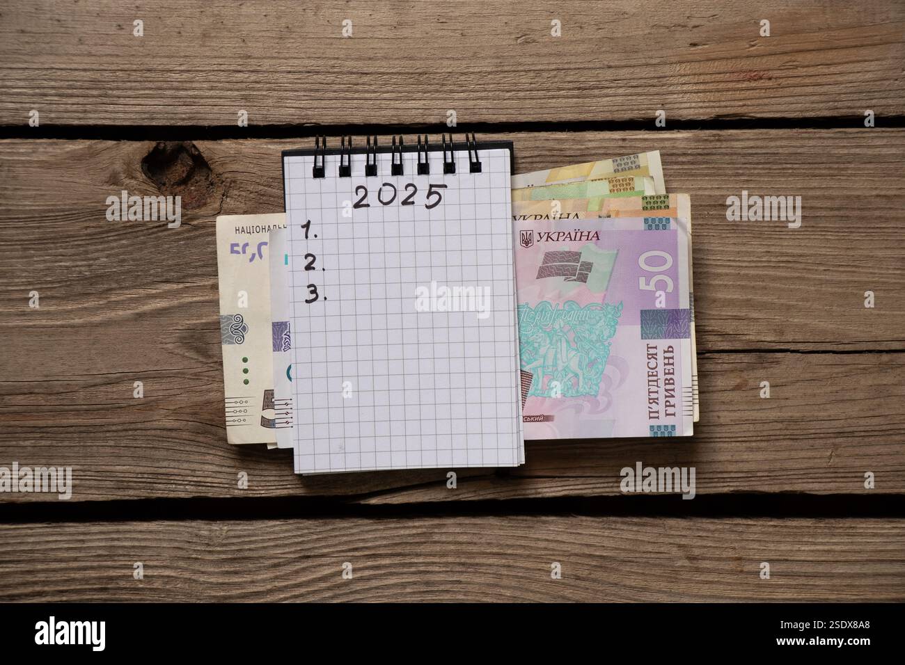 2025 e 123 sono scritti in un quaderno e hrivnia Ucraina, che si trova su un tavolo di legno, i piani per il nuovo anno, scrivono i piani Foto Stock