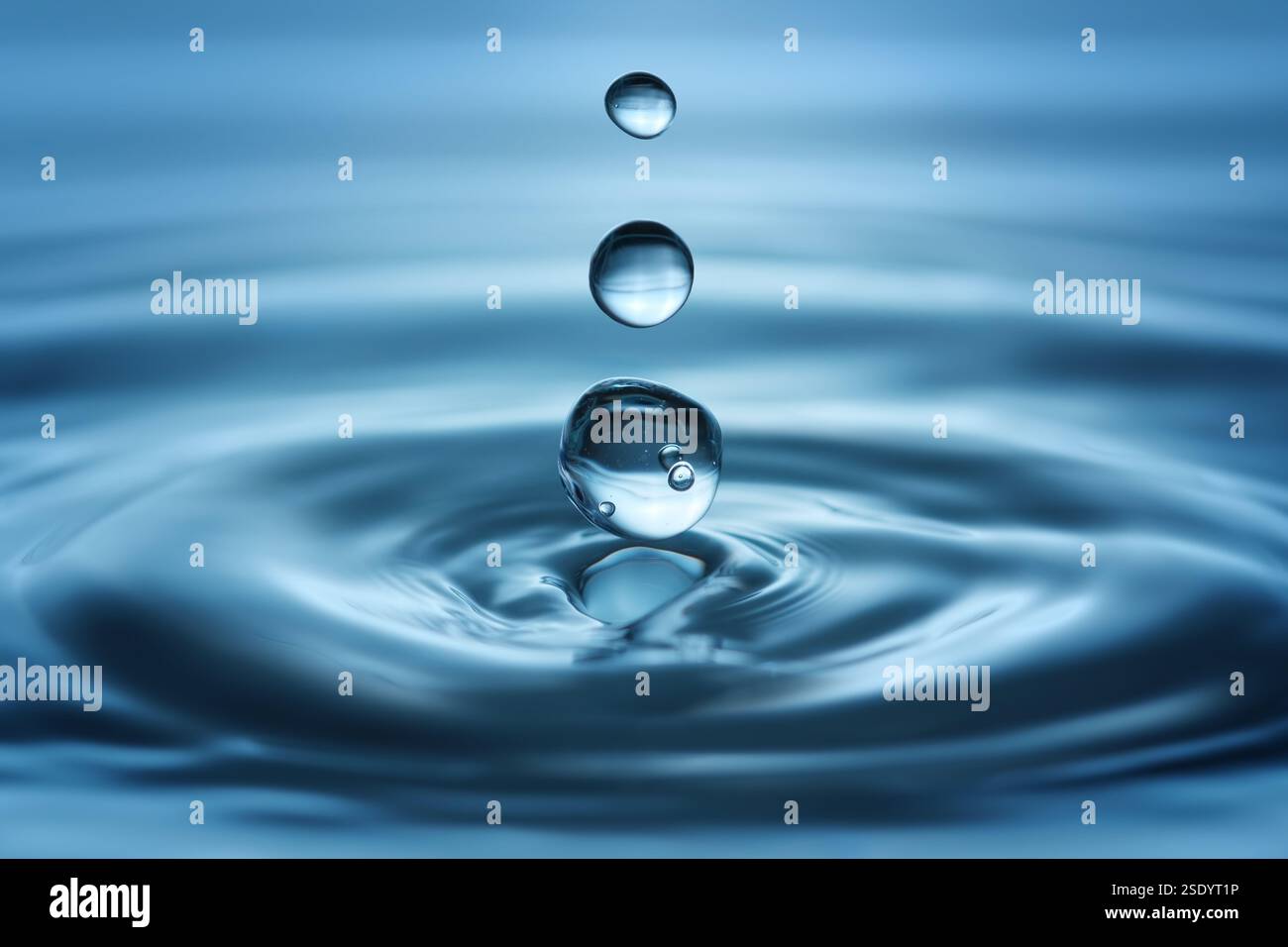 Tre gocce limpide che cadono nell'acqua blu e creano increspature, riprese in studio Foto Stock