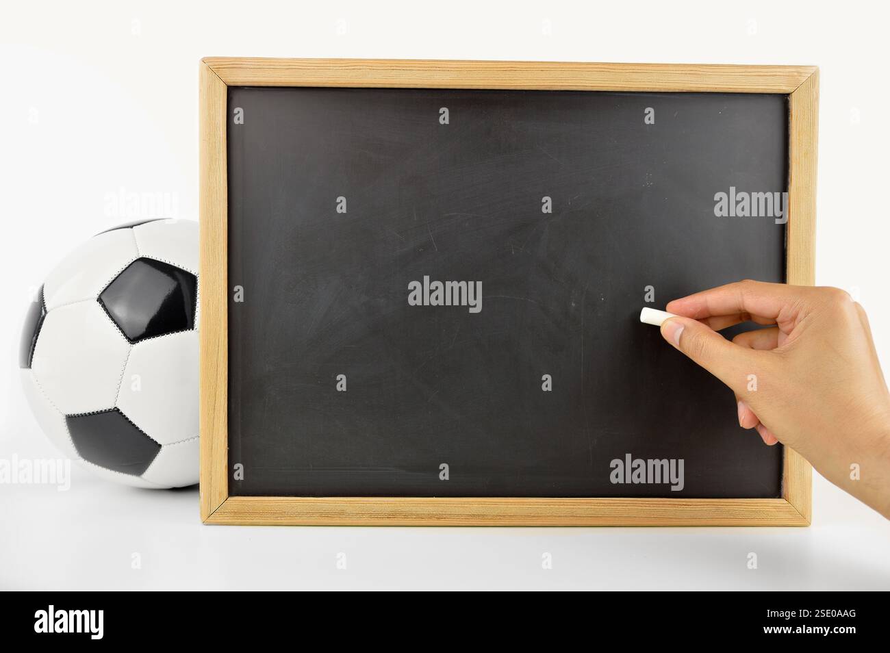 mano di un allenatore di calcio che disegna con gesso bianco su lavagna vuota con spazio imbottito accanto alla palla da calcio isolata su sfondo bianco Foto Stock