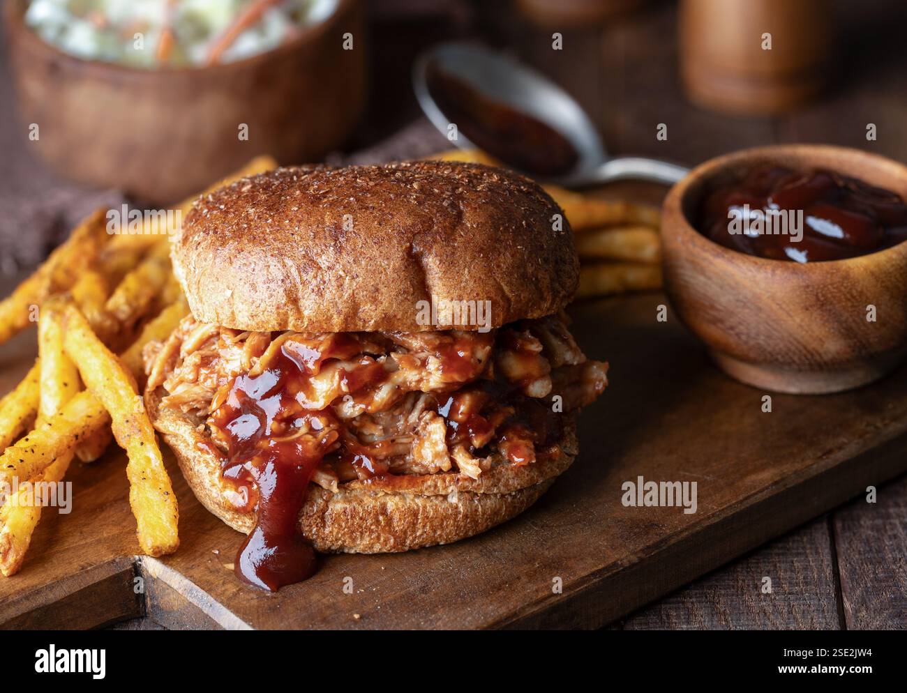 Sandwich di pollo alla griglia su panino integrale con patatine fritte su tagliere di legno e insalata di cavolo sullo sfondo Foto Stock
