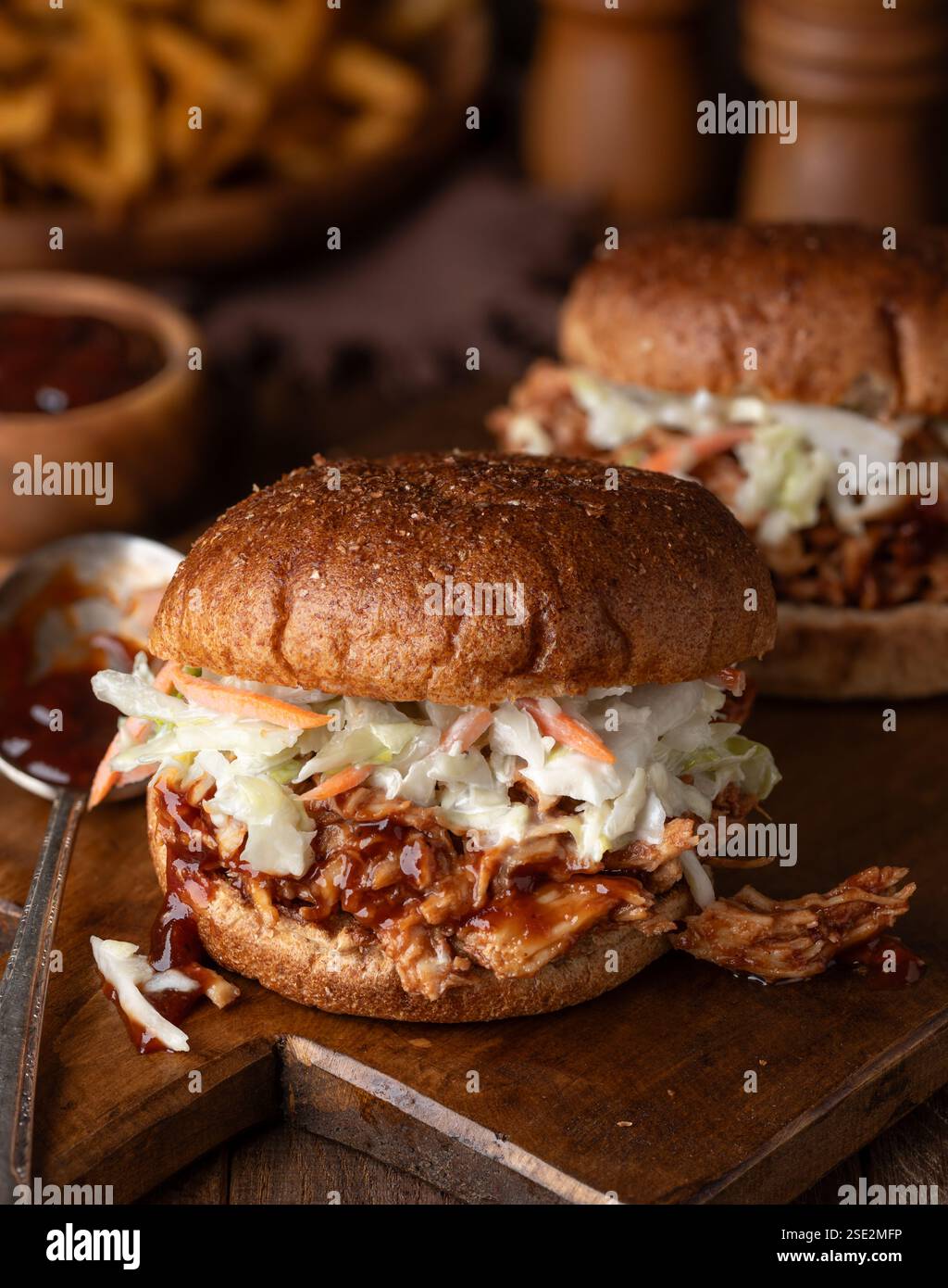 Il pollo alla griglia e i sandwichs di cavolo sul panino integrale su un tagliere di legno con patatine fritte sullo sfondo Foto Stock