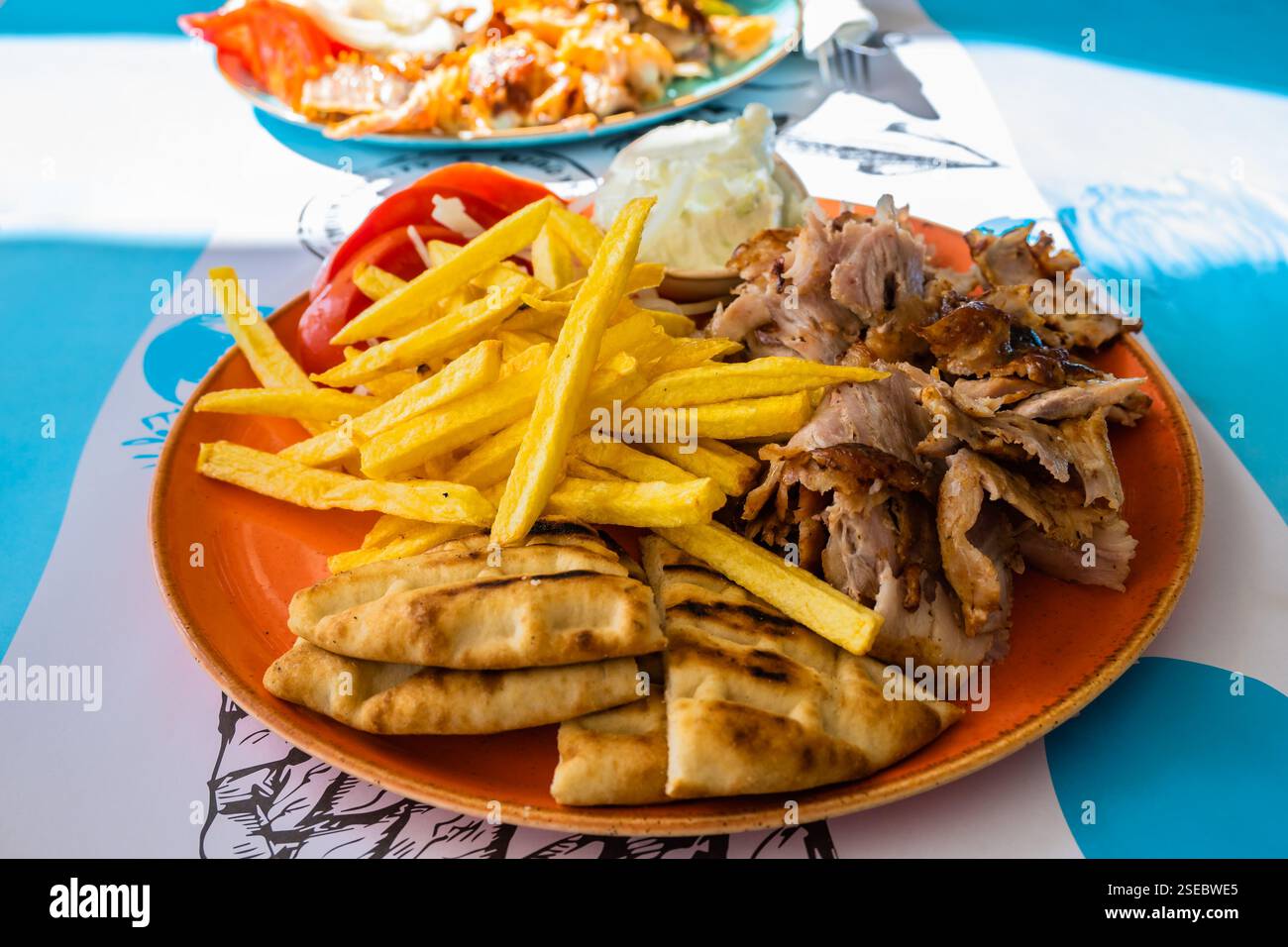 Piatto con carne Gyros, pane pita, pomodori e patatine fritte in tavola nel ristorante greco, porto di Adamas, isola di Milos, Cicladi, Grecia Foto Stock