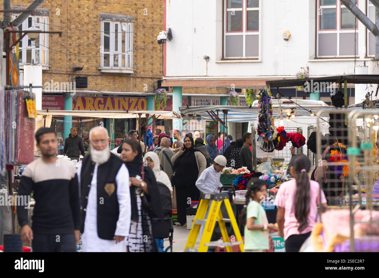 Gli amanti dello shopping nella vivace Chrisp Street, Poplar, East London, curiosano tra le bancarelle che vendono articoli per la casa e prodotti. Comunità diversificata. Foto Stock