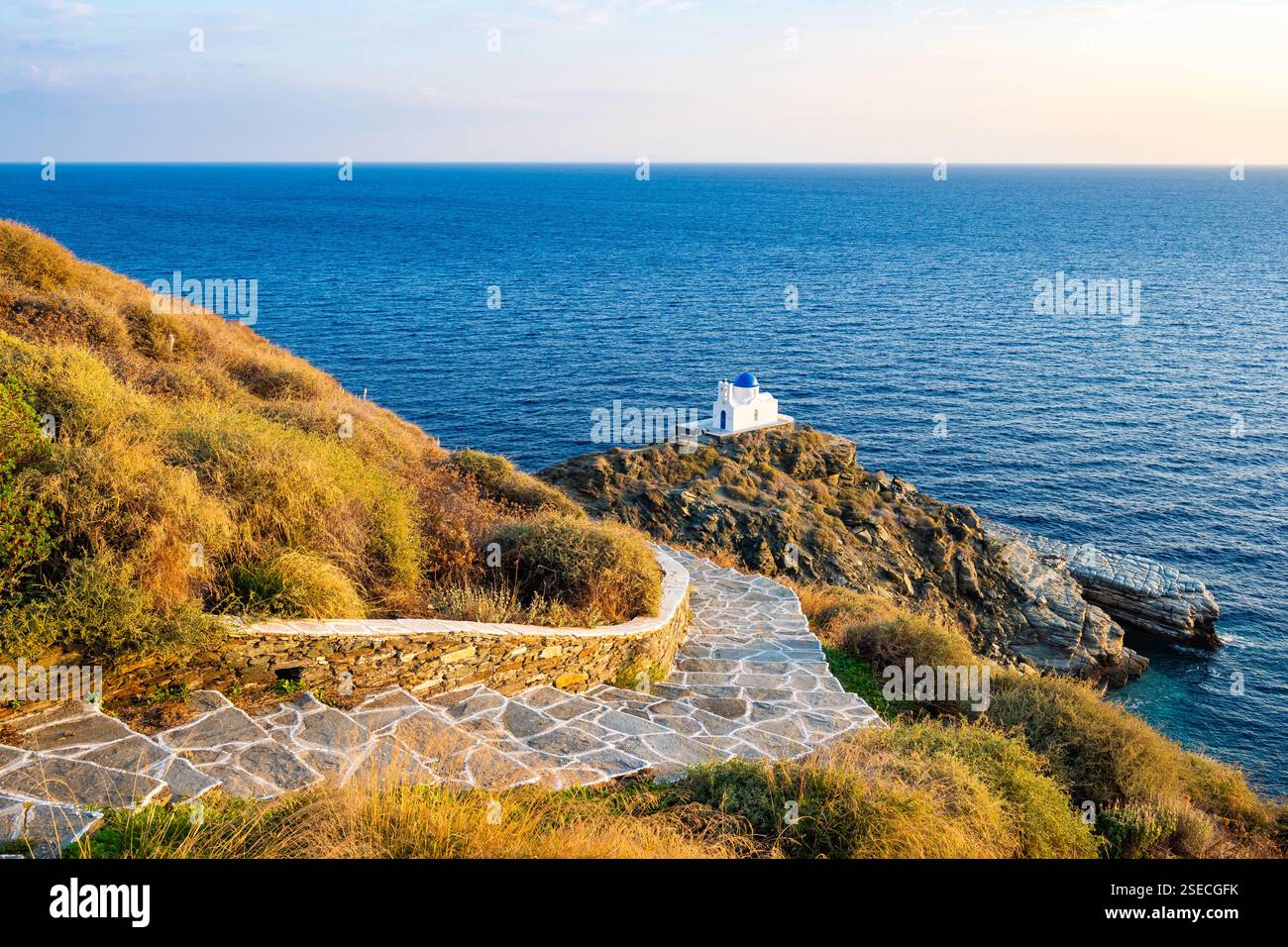 Sentiero costiero con scalini per una piccola chiesa costruita su rocce e mare blu sullo sfondo nel villaggio di Kastro all'alba, isola di Sifnos, Grecia Foto Stock