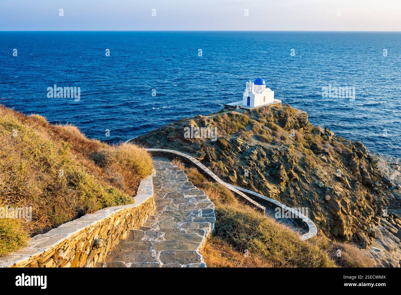 Sentiero costiero con scalini per una piccola chiesa costruita su rocce e mare blu sullo sfondo nel villaggio di Kastro, isola di Sifnos, Grecia Foto Stock