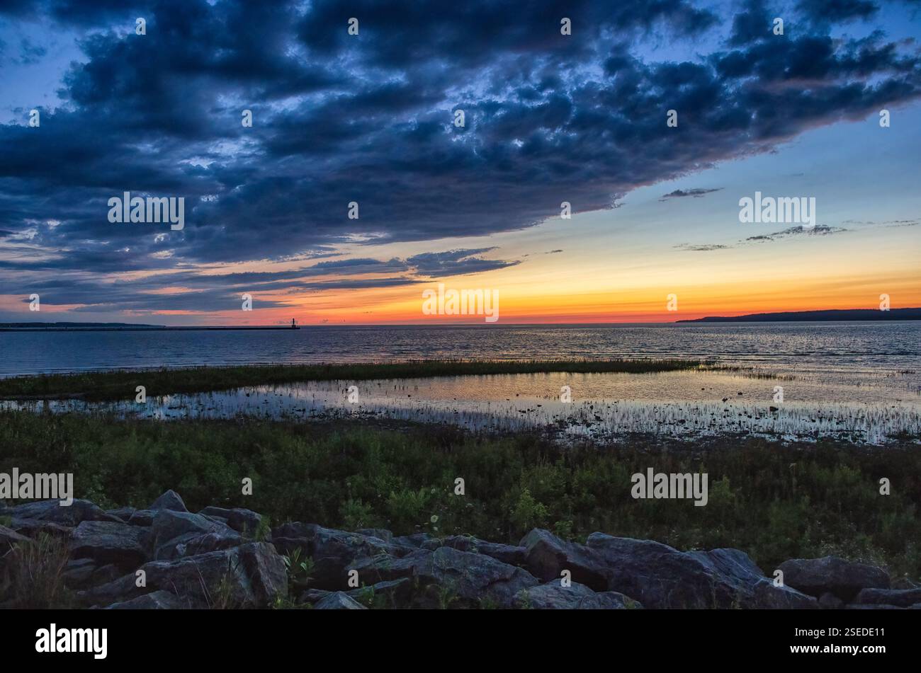 Un vibrante tramonto sul lago Michigan con un faro lontano all'orizzonte, che si riflette sull'acqua con spettacolari nuvole sopra. Foto Stock