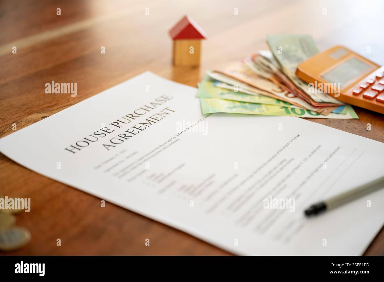 Un accordo di acquisto di una casa su un tavolo di legno con contanti, una calcolatrice, una penna e un piccolo modello di casa, simboleggiando gli investimenti immobiliari e finanziari Foto Stock