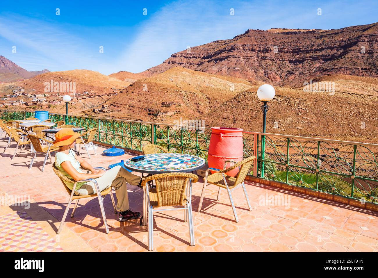 Giovane turista seduta sulla terrazza del ristorante e guarda le montagne dell'Atlante sulla strada per il passo tizi n'Tichka nella città di Tisseldei, Marocco, Afri Nord Foto Stock
