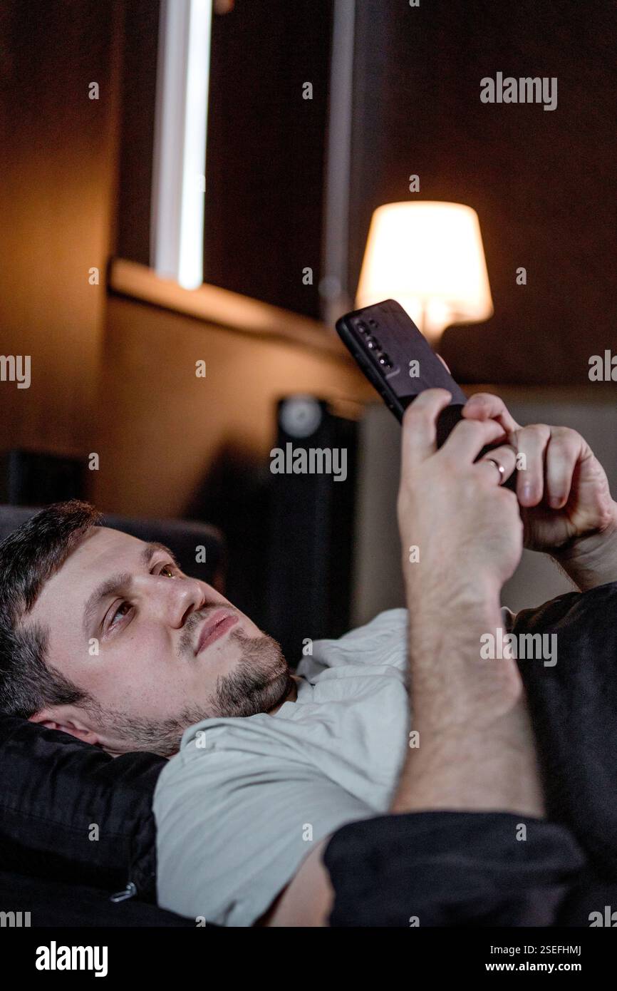 Giovane sdraiato a letto di notte e che guarda lo schermo del telefono cellulare. Foto Stock