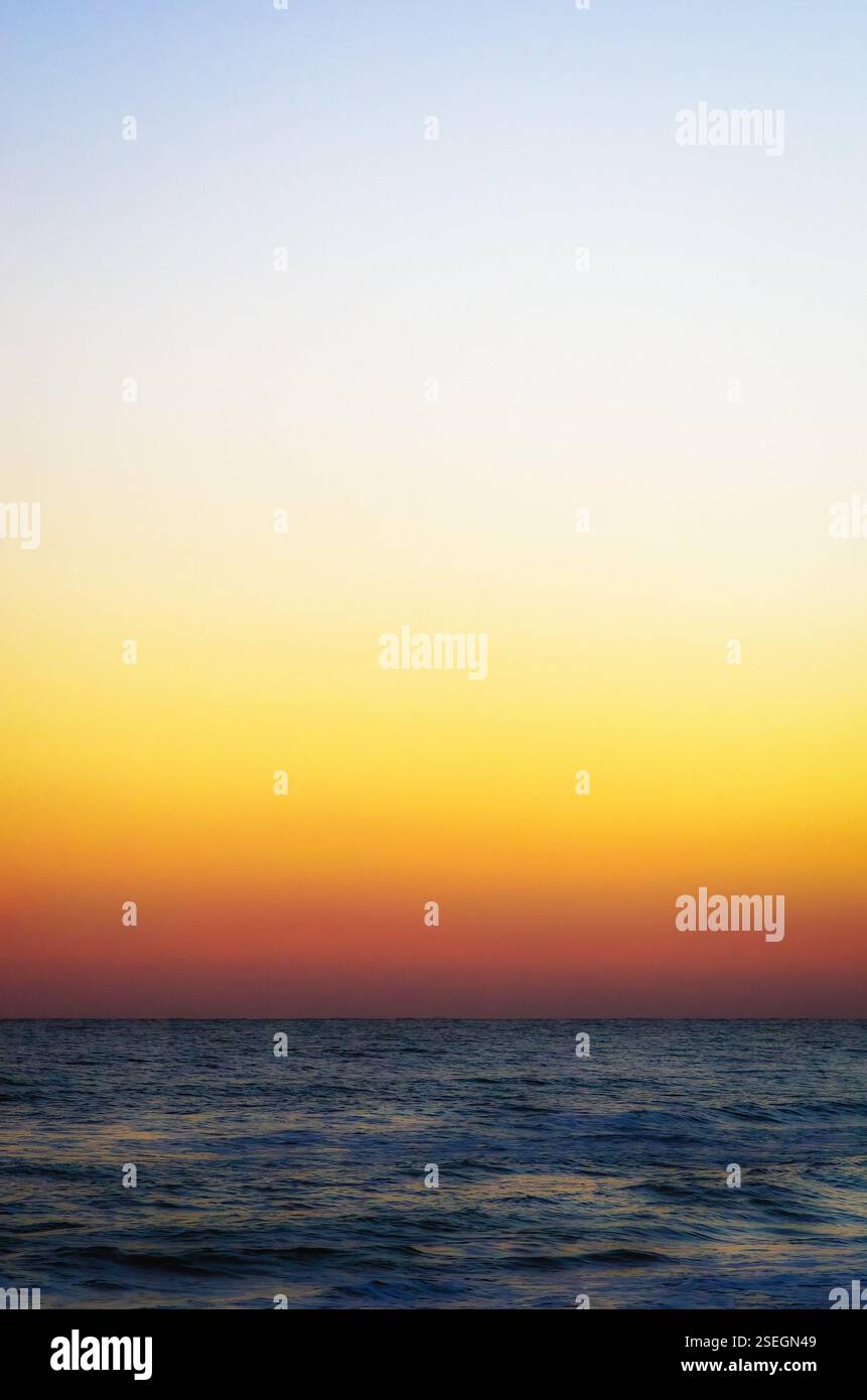 Una tranquilla alba sulla spiaggia atlantica con un cielo in pendenza che si fonde nelle calme acque oceaniche, catturando una tranquilla mattinata costiera Foto Stock