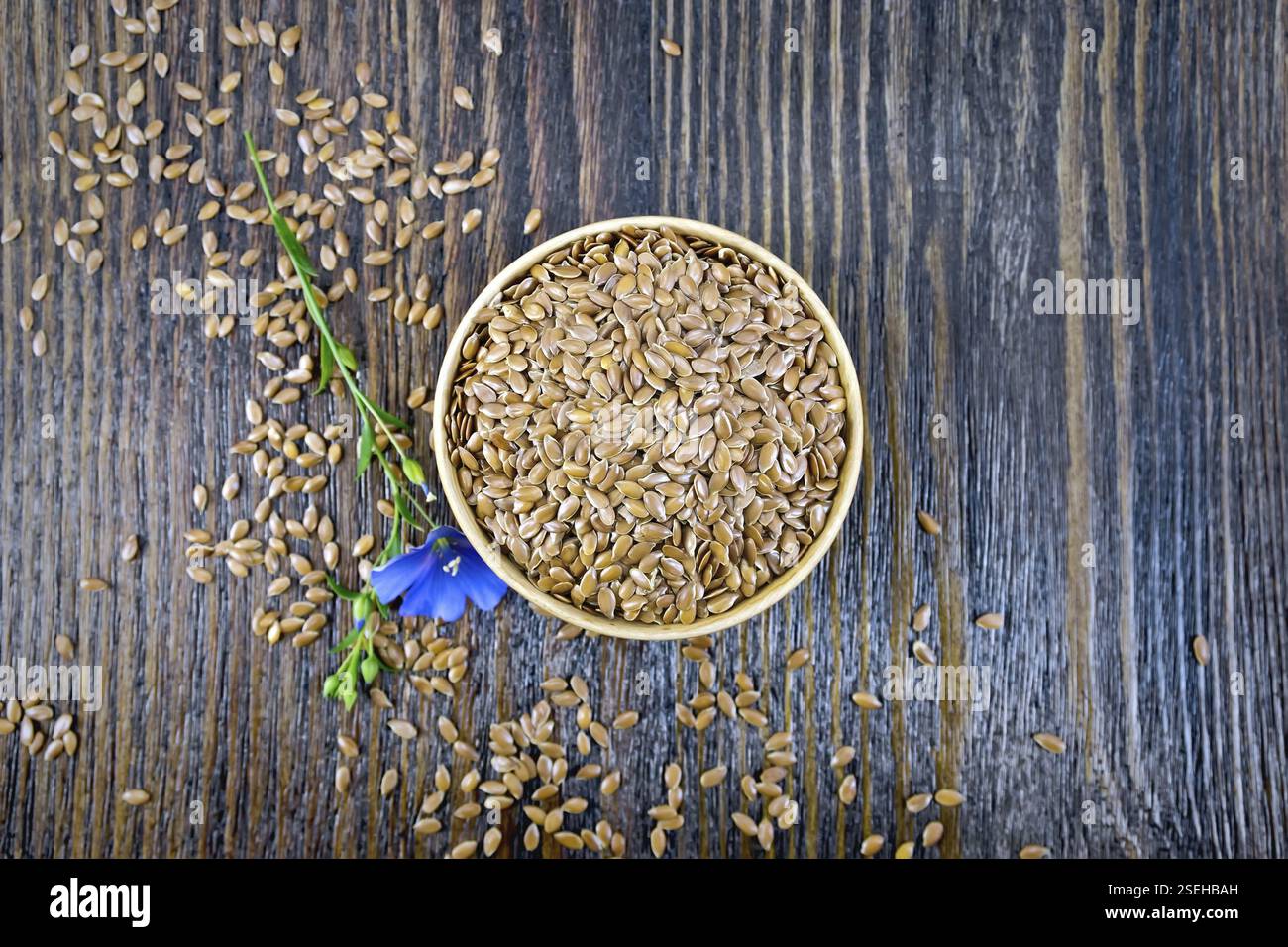 Semi di lino marrone in una ciotola, lino blu fiore su una tavola di legno del fondo da sopra Foto Stock