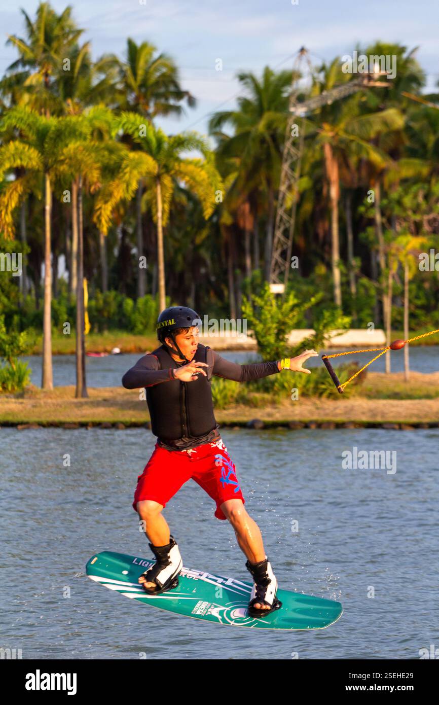 Un giovane adulto maschio wakeboarding a tutta velocità in un parco di wakeboard a Davao City, Filippine, catturato a metà azione Foto Stock