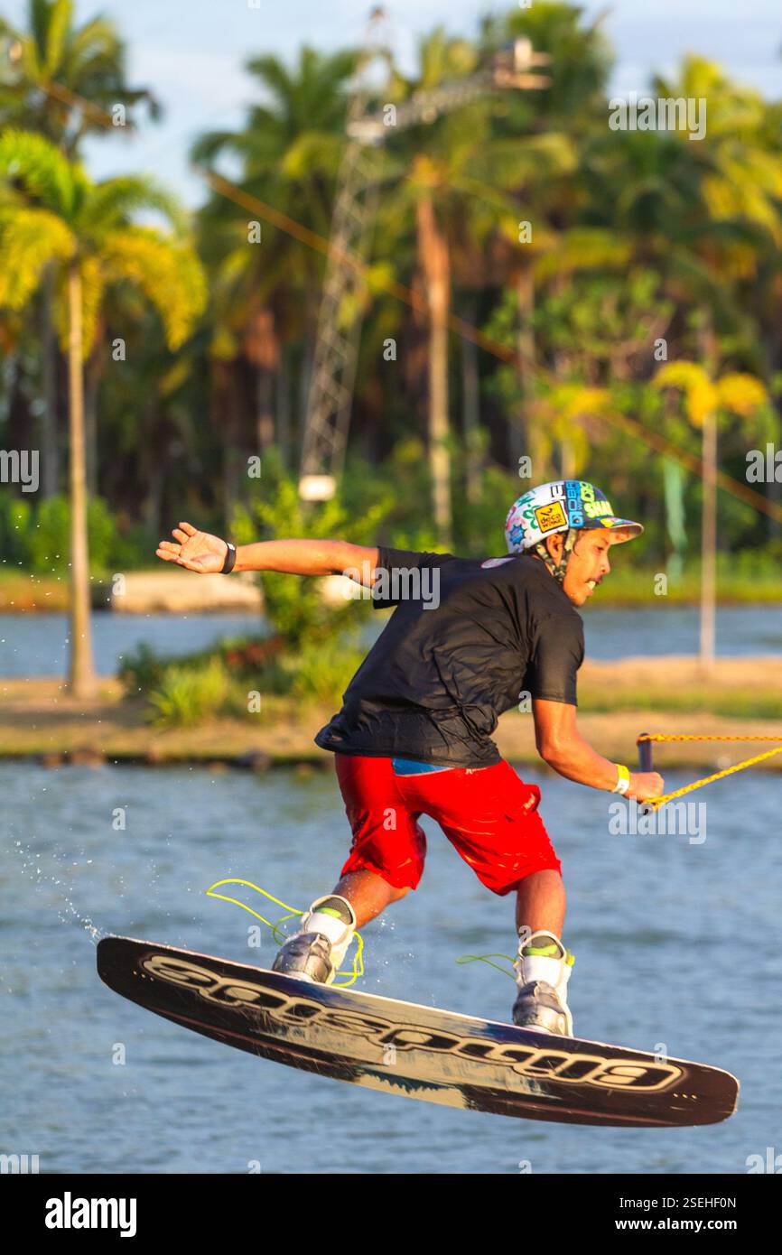 Un giovane adulto maschio wakeboarding a tutta velocità in un parco di wakeboard a Davao City, Filippine, catturato a metà azione Foto Stock