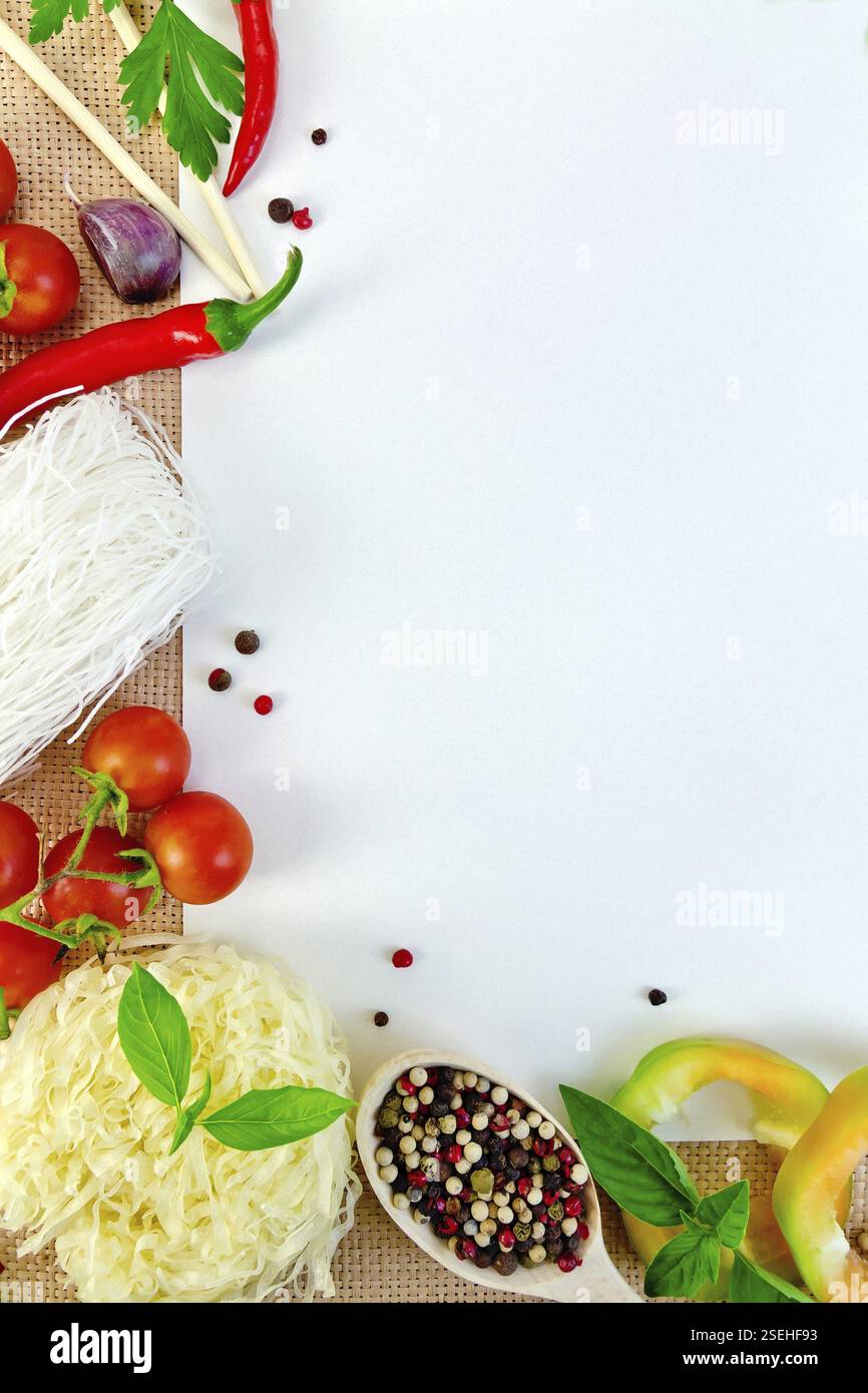 Cornice di spaghetti di riso, pomodori, peperoni, basilico, prezzemolo e aglio, libro bianco su un sacco Foto Stock