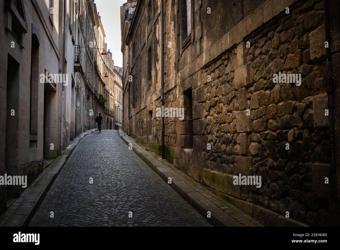Vista orizzontale di una stretta strada del centro storico di Bordeaux, con un uomo che cammina sul marciapiede circondato dalle mura di vecchi edifici in pietra Foto Stock