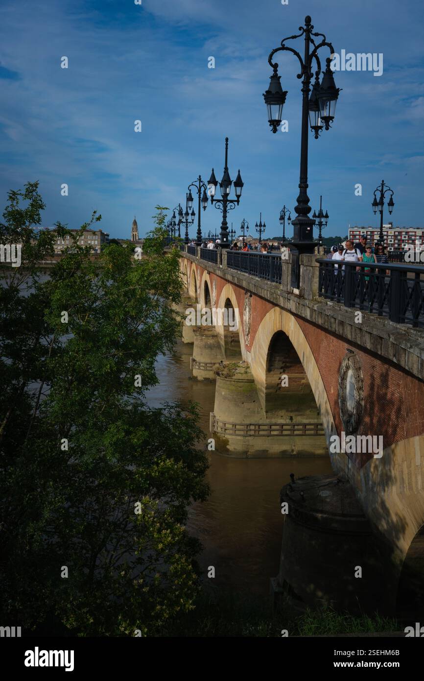 Vista prospettica verticale su un ponte di pietre e mattoni sul fiume Garonna, con guglia della chiesa sullo sfondo, con lampioni in vecchio stile Foto Stock