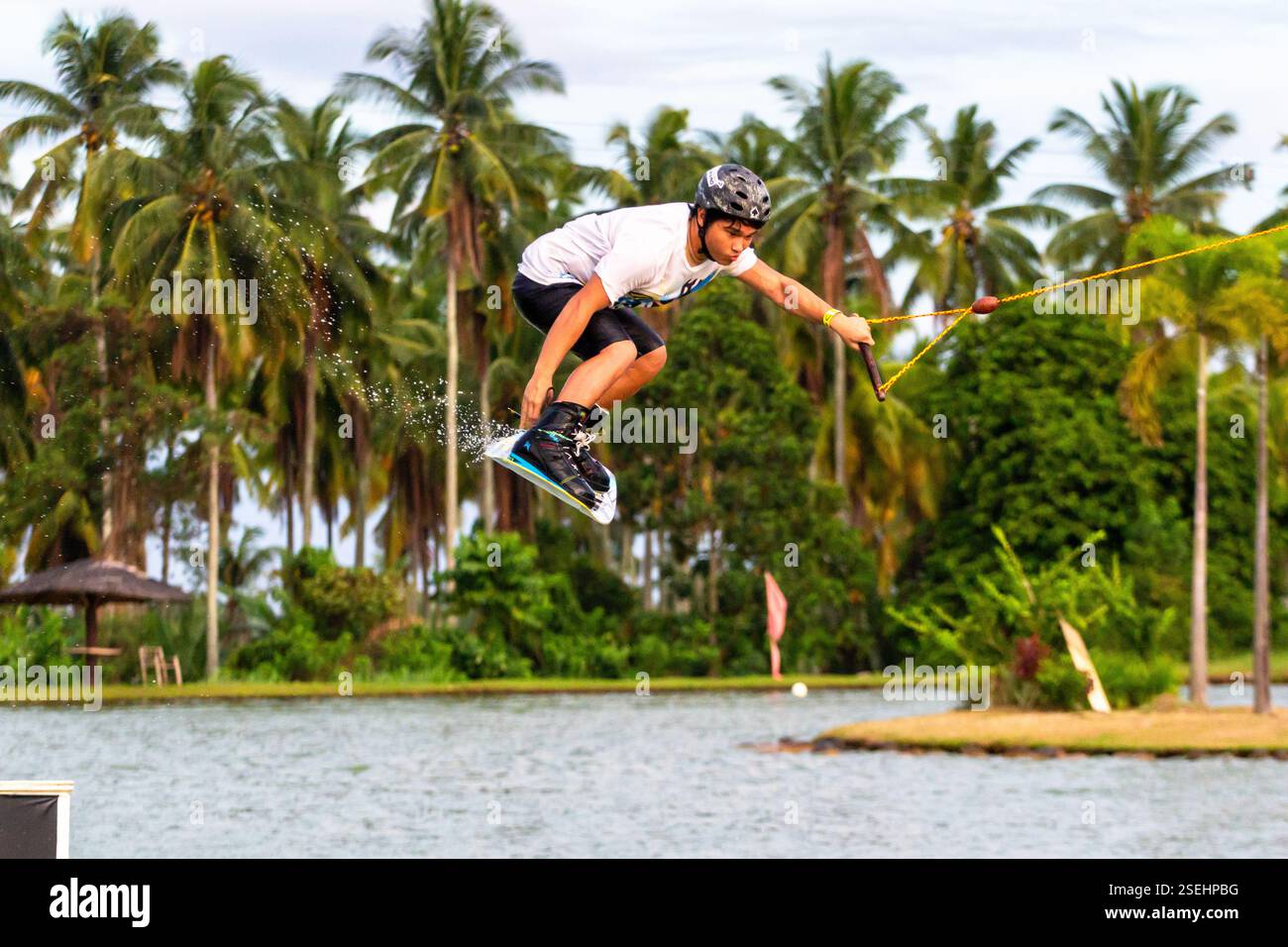 Un giovane adulto maschio wakeboarding a tutta velocità in un parco di wakeboard a Davao City, Filippine, catturato a metà azione Foto Stock