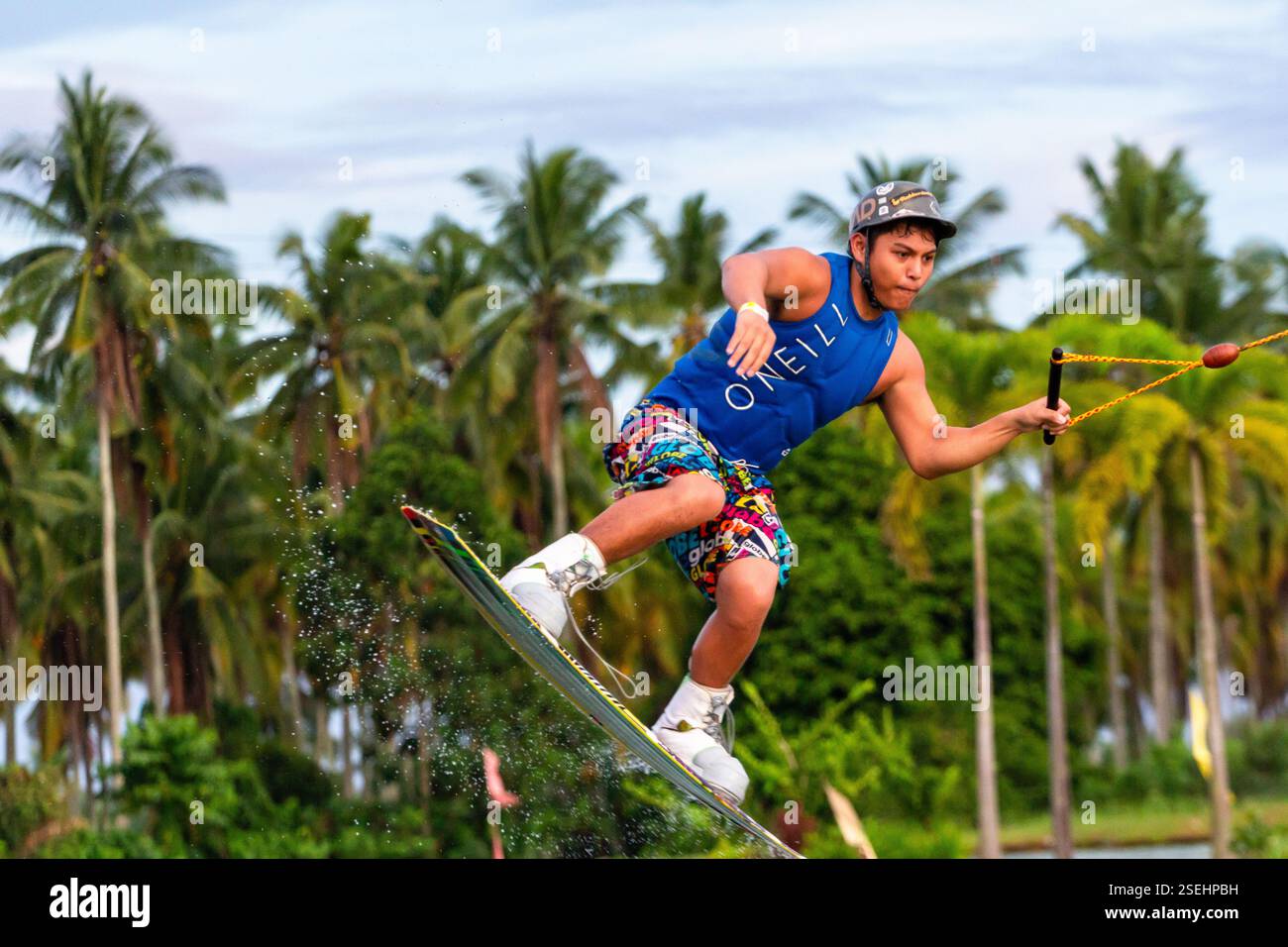 Un giovane adulto maschio wakeboarding a tutta velocità in un parco di wakeboard a Davao City, Filippine, catturato a metà azione Foto Stock