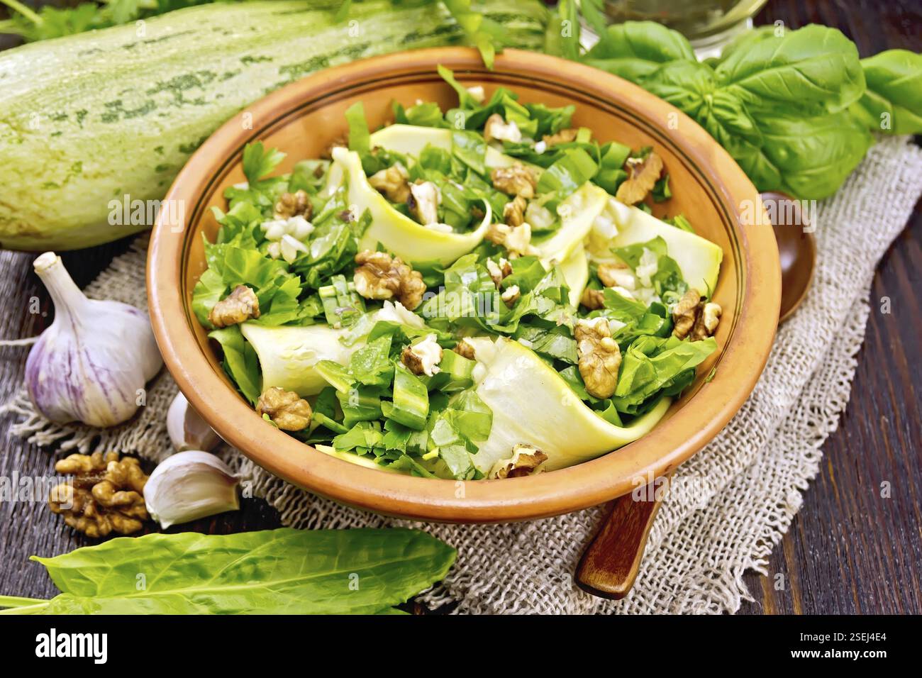 Insalata di giovani zucchine, sorrel, aglio e i dadi, condito con olio vegetale in una piastra sul tovagliolo del sacco su uno sfondo di legno scuro board Foto Stock