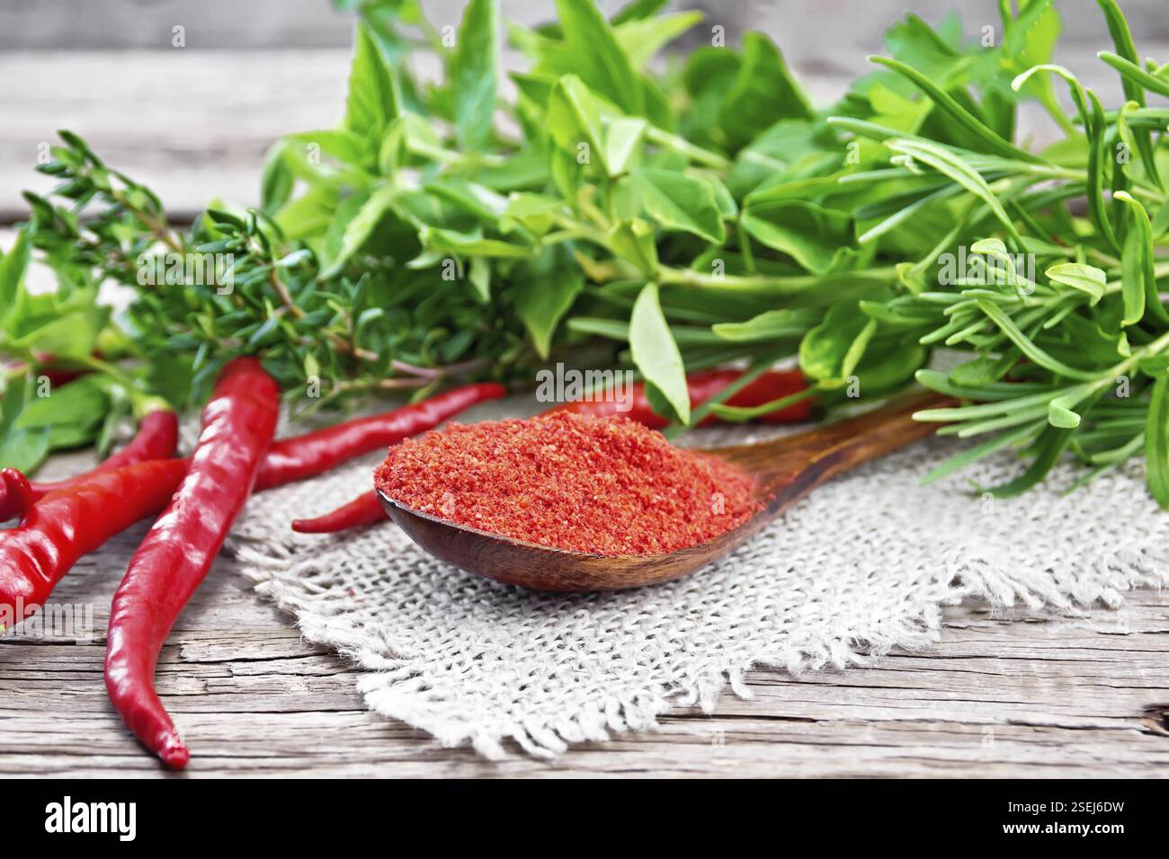 Suolo caldo rosso pepe in un cucchiaio su tela, cialde di peperoncino piccante e verdi su sfondo di una vecchia scheda di legno Foto Stock
