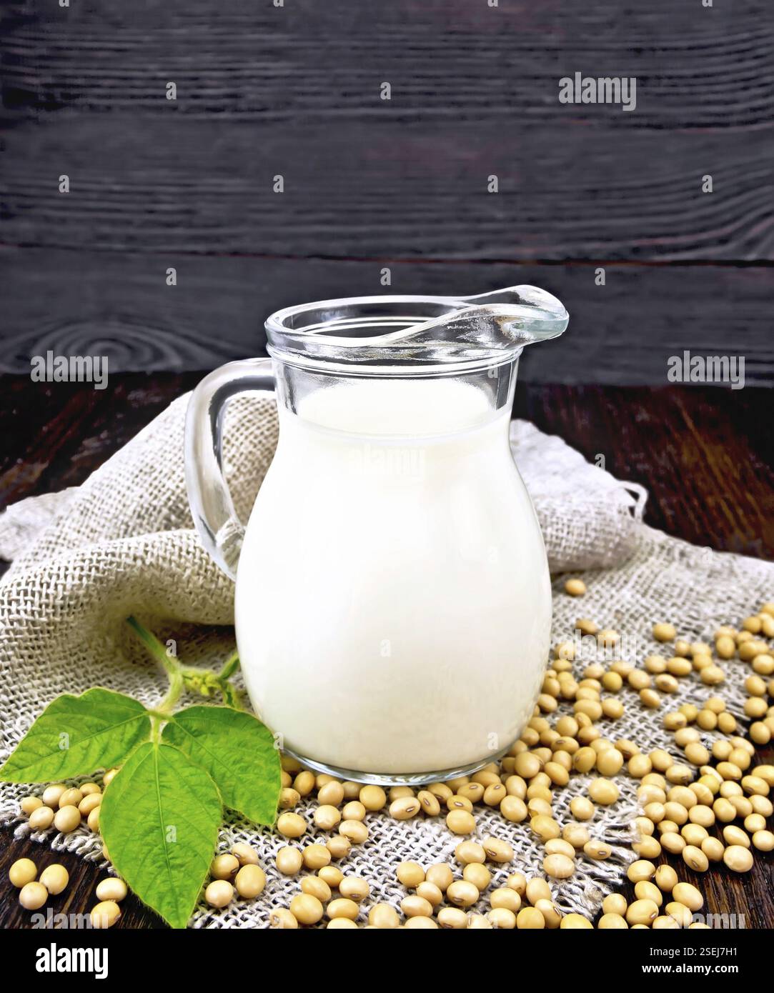Il latte di soia in una brocca, foglia verde, soia su un tovagliolo di tela su una tavola di legno sfondo Foto Stock