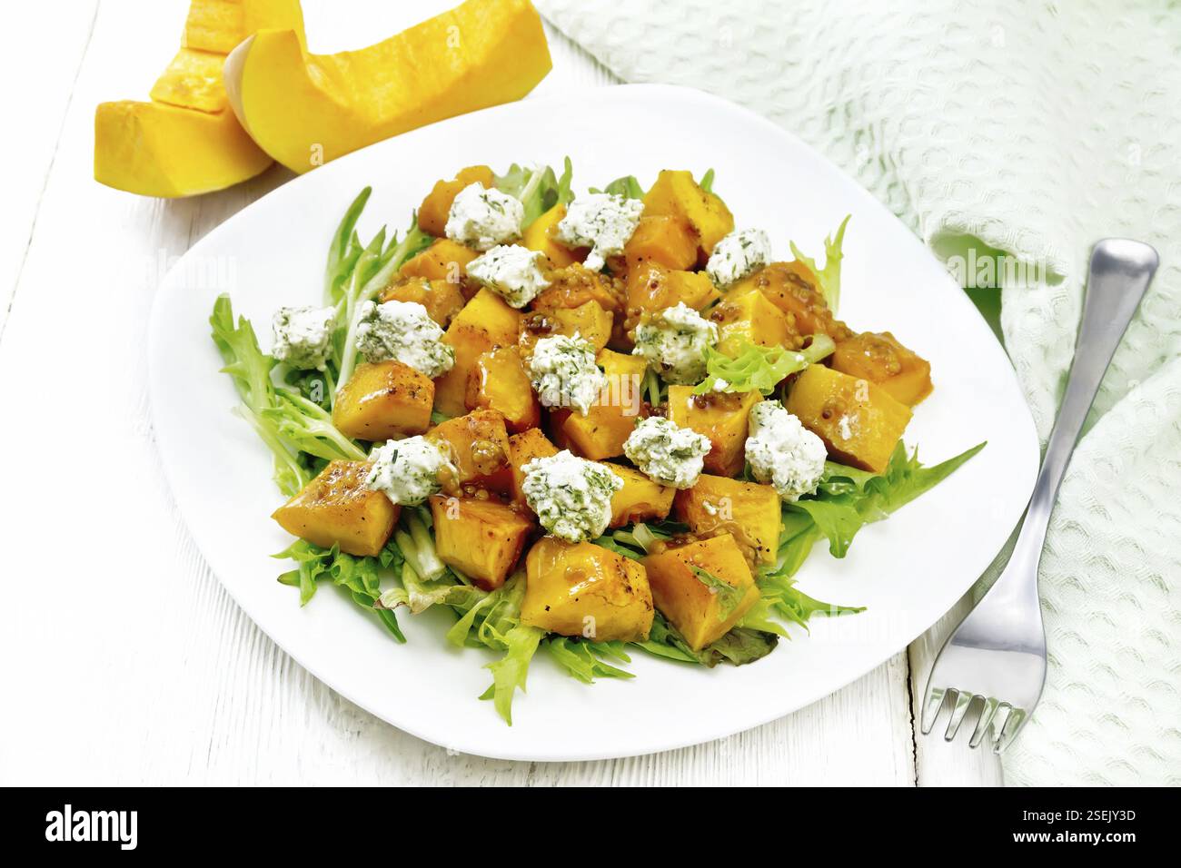 Insalata di zucca al forno, rucola con palle di formaggio salato, condita con miele, senape, aglio e olio vegetale in un piatto, asciugamano e forchetta su legno Foto Stock