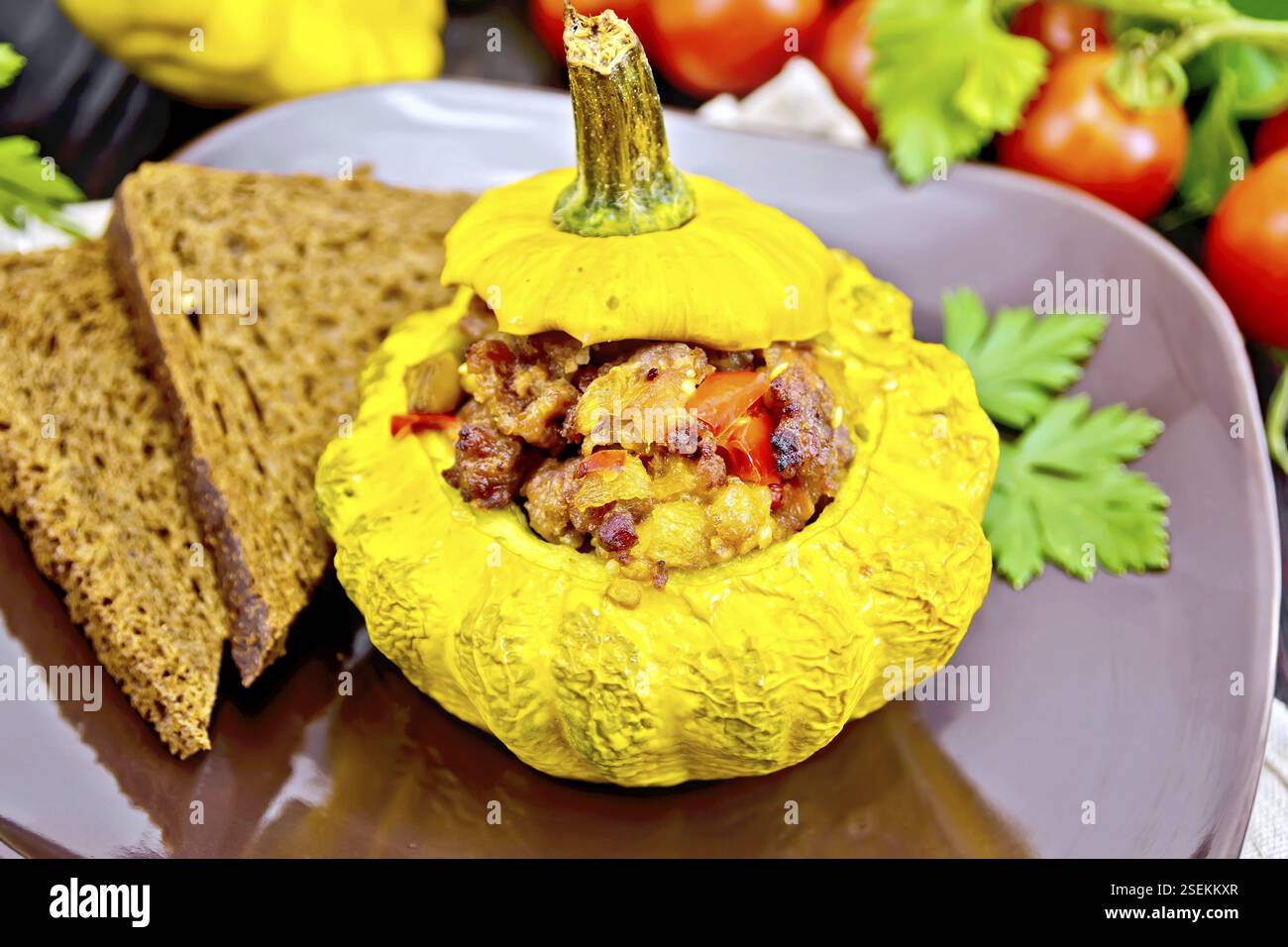 Squash giallo con ripieno di carne, pomodori e peperoni, pane in una piastra marrone, i pomodori, il prezzemolo su tavole di legno sfondo Foto Stock