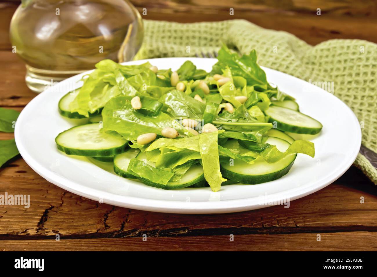 Insalata di spinaci, cetrioli freschi, rukkola insalata, dadi di cedro e cipolline, condito con olio vegetale su una piastra, igienico e forcella su un marrone b Foto Stock